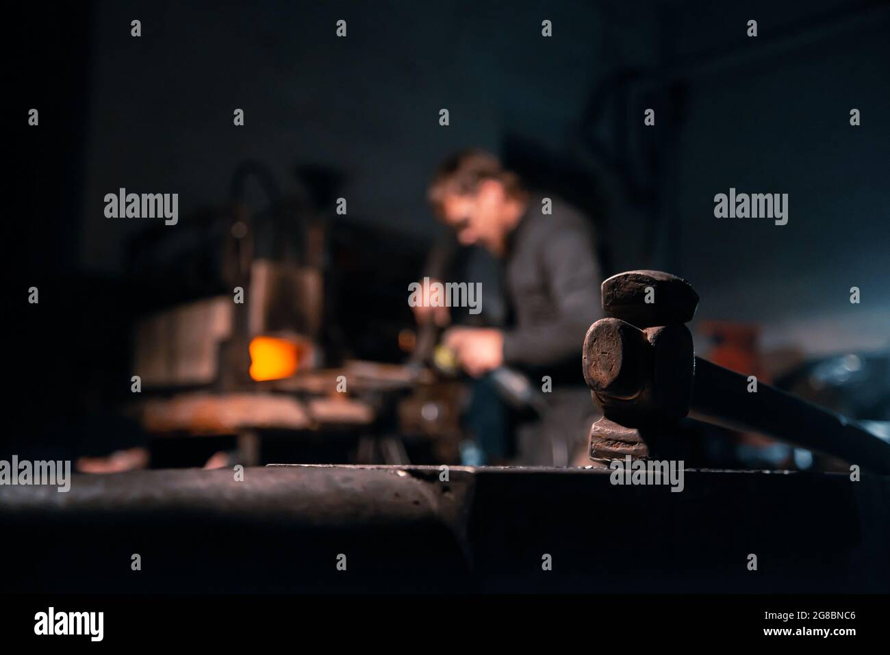 Incudine con un martello in primo piano, e fabbro sullo sfondo. Foto Stock
