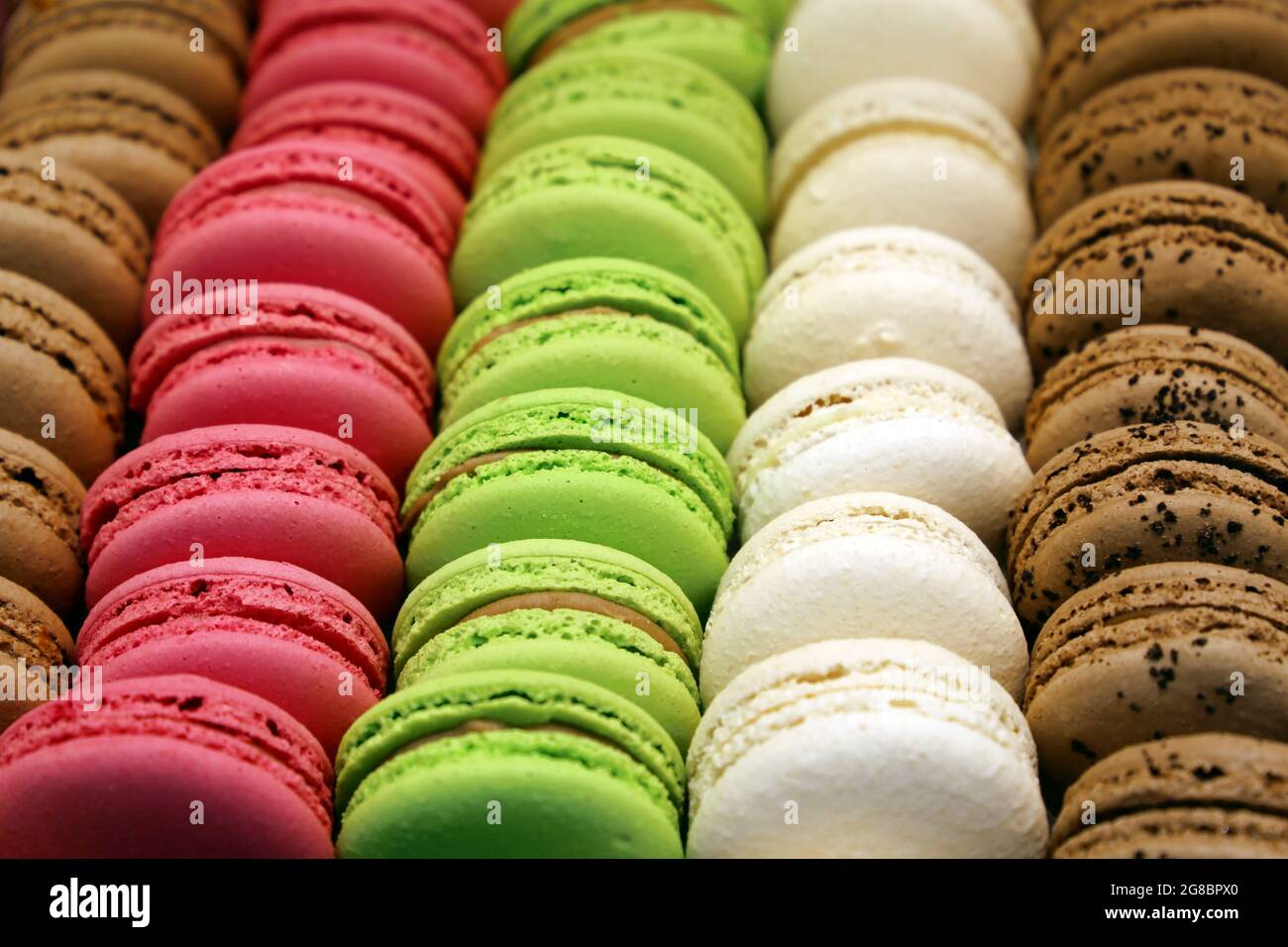 Macaroni in fila ravvicinata, colorato sfondo dolce. Biscotti alla fragola, alla vaniglia e alle mandorle al cioccolato con ripieno in un negozio Foto Stock