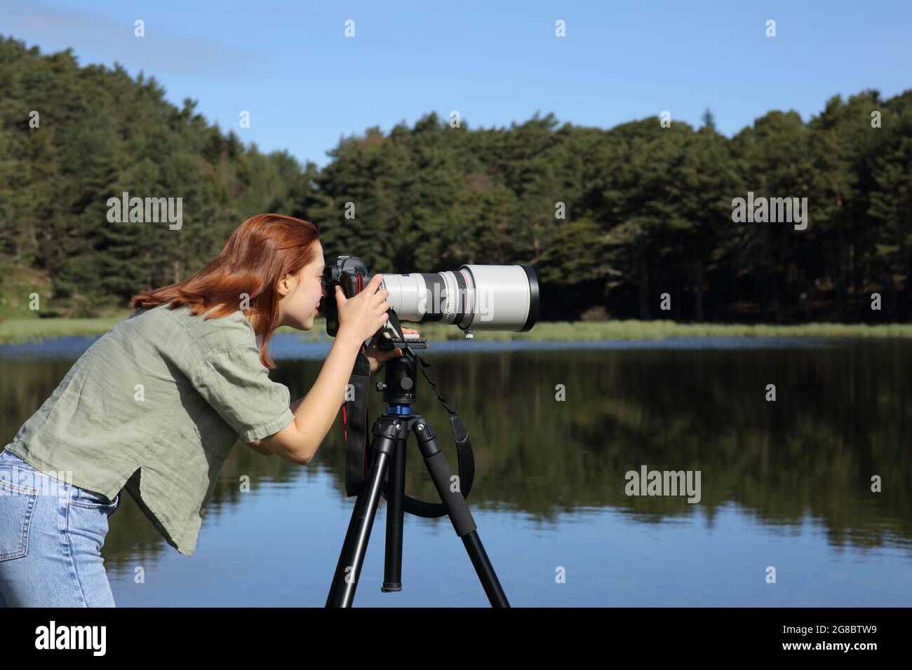 Ritratto in vista laterale di un fotografo che scatta foto con teleobiettivo e fotocamera dslr in un lago Foto Stock