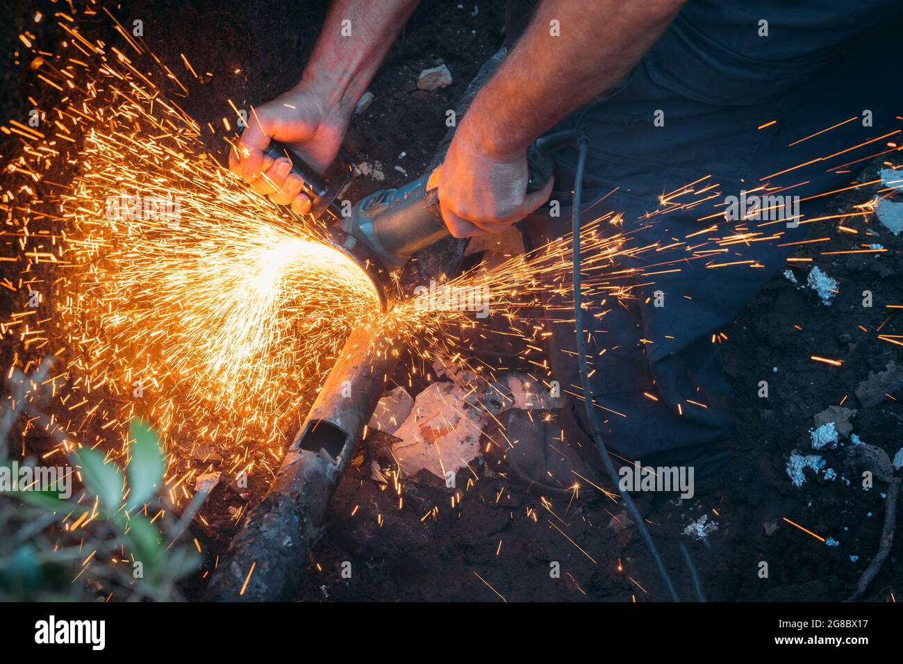 Il lavoratore taglia il tubo del gas con il macinacaffè e molte scintille volano da vicino. Foto Stock