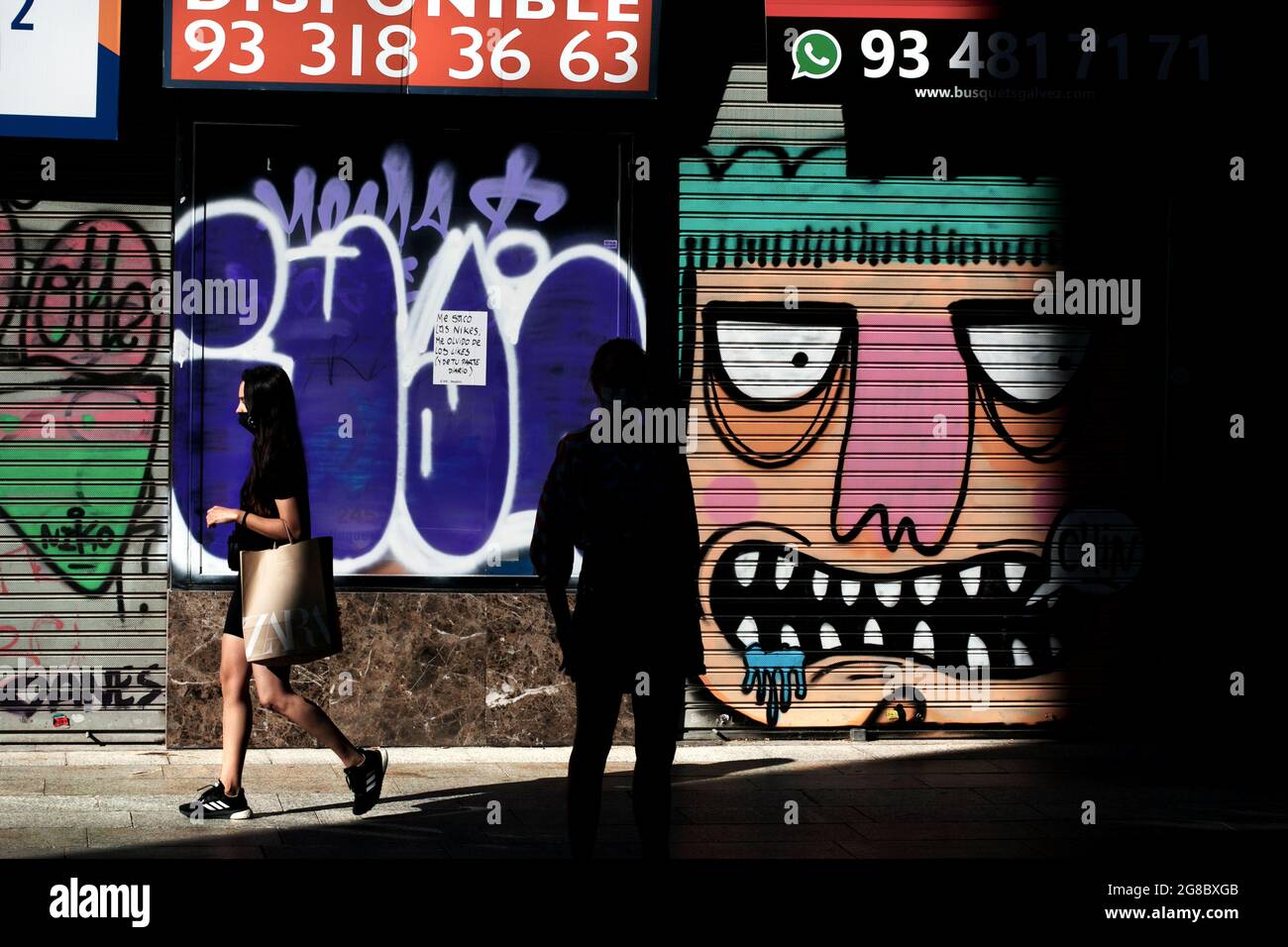 Donna mascherata che passa davanti ai graffiti in strada, Barcellona, Spagna. Foto Stock