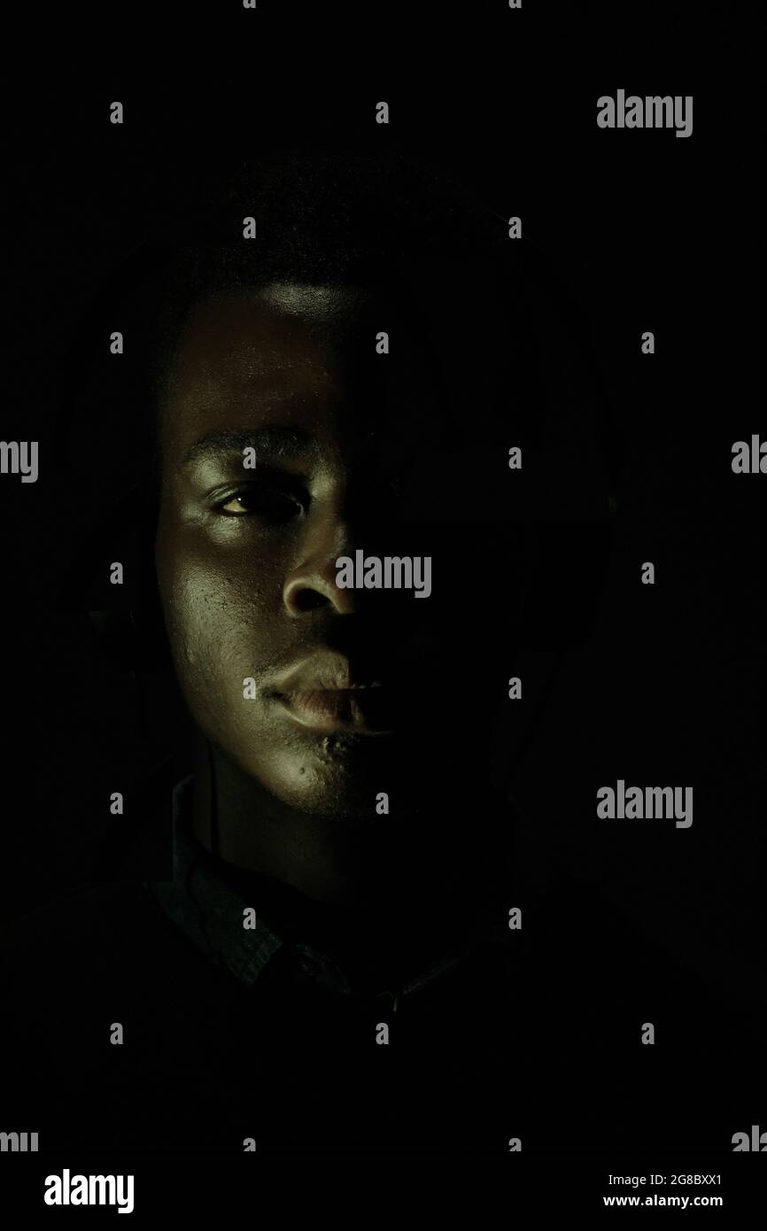 Il volto di un giovane africano nero è circondato dalle tenebre. Simbolo del movimento della materia delle vite nere. Foto Stock