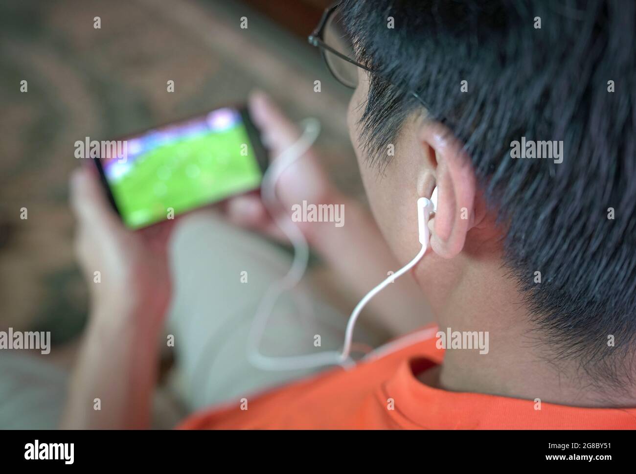 Uomo che guarda il calcio e lo sport in streaming sul telefono cellulare. Messa a fuoco selezionata sugli auricolari. Foto Stock