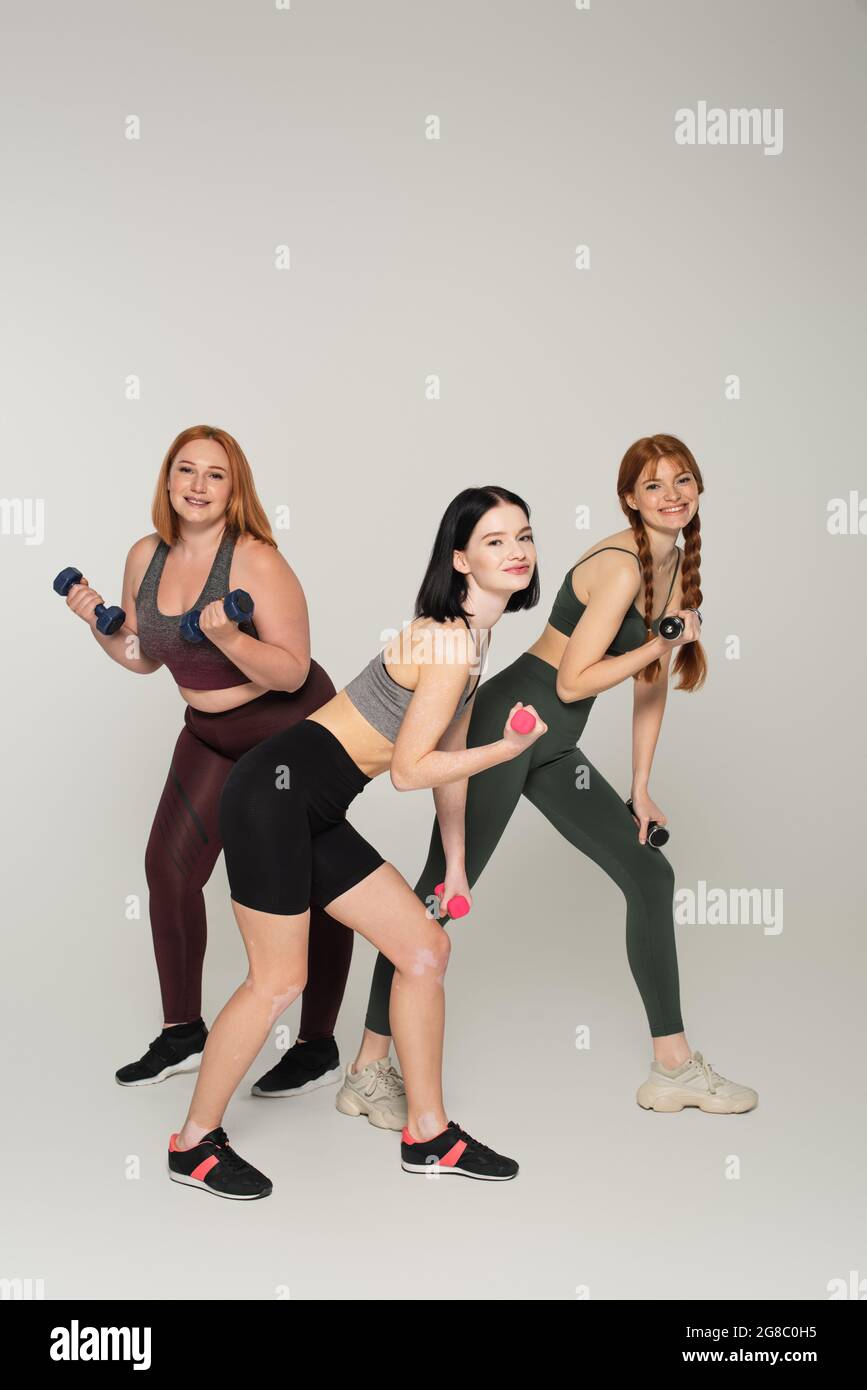 Corpo positivo donne che si esercitano con manubri su sfondo grigio Foto Stock
