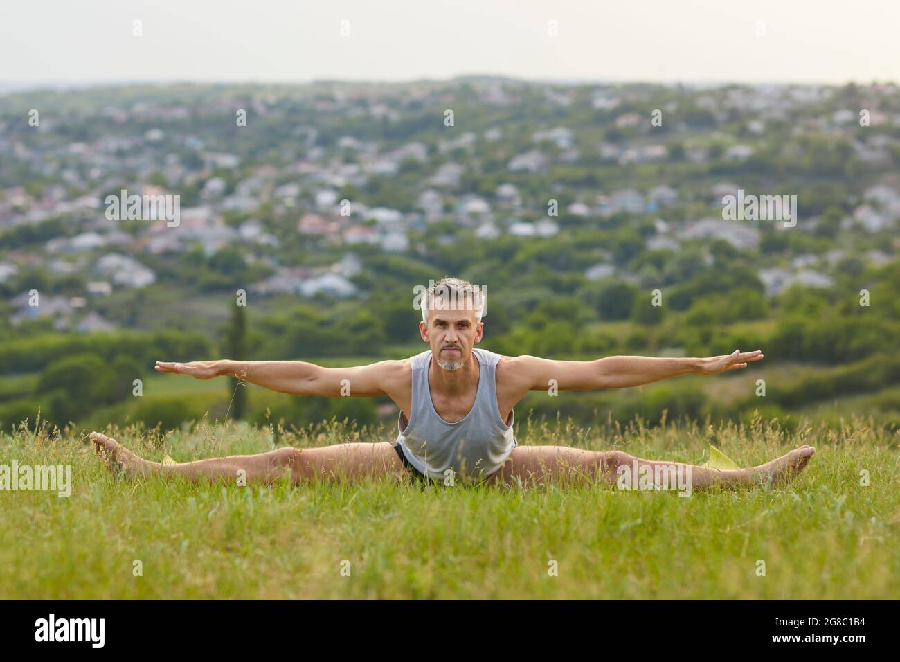 Yogi maschile fiducioso che pratica la curva in avanti e l'esercizio sulle gambe in verde prato estivo Foto Stock