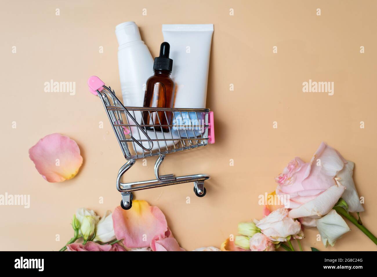 Vasetti cosmetici bianchi con crema e siero idratante in bottiglia marrone si trovano in un carrello per lo shopping su sfondo beige. Shopping online. Foto Stock