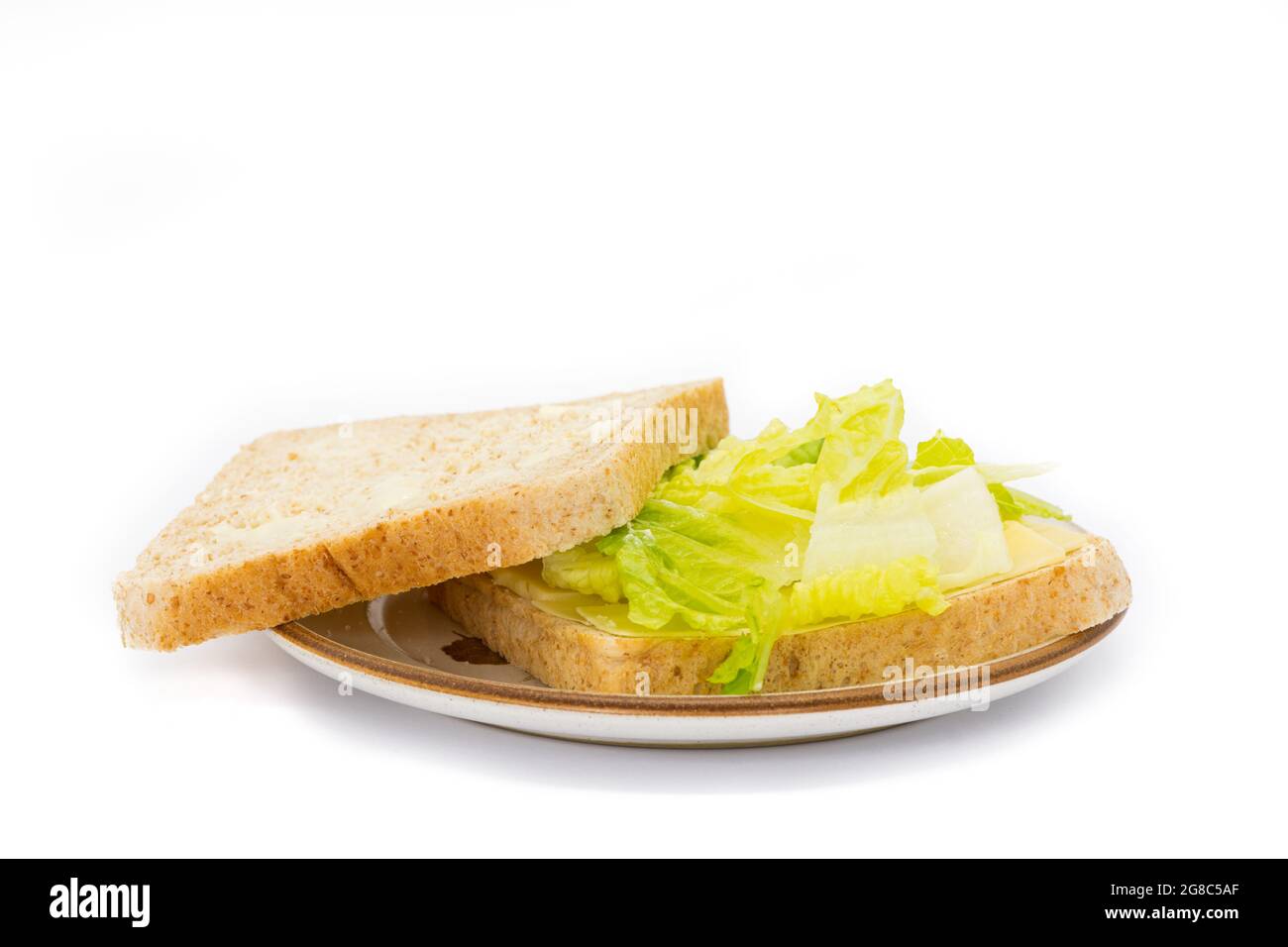Primo piano di un sacco di pane marrone con lattuga e formaggio su un piatto e su fondo bianco Foto Stock