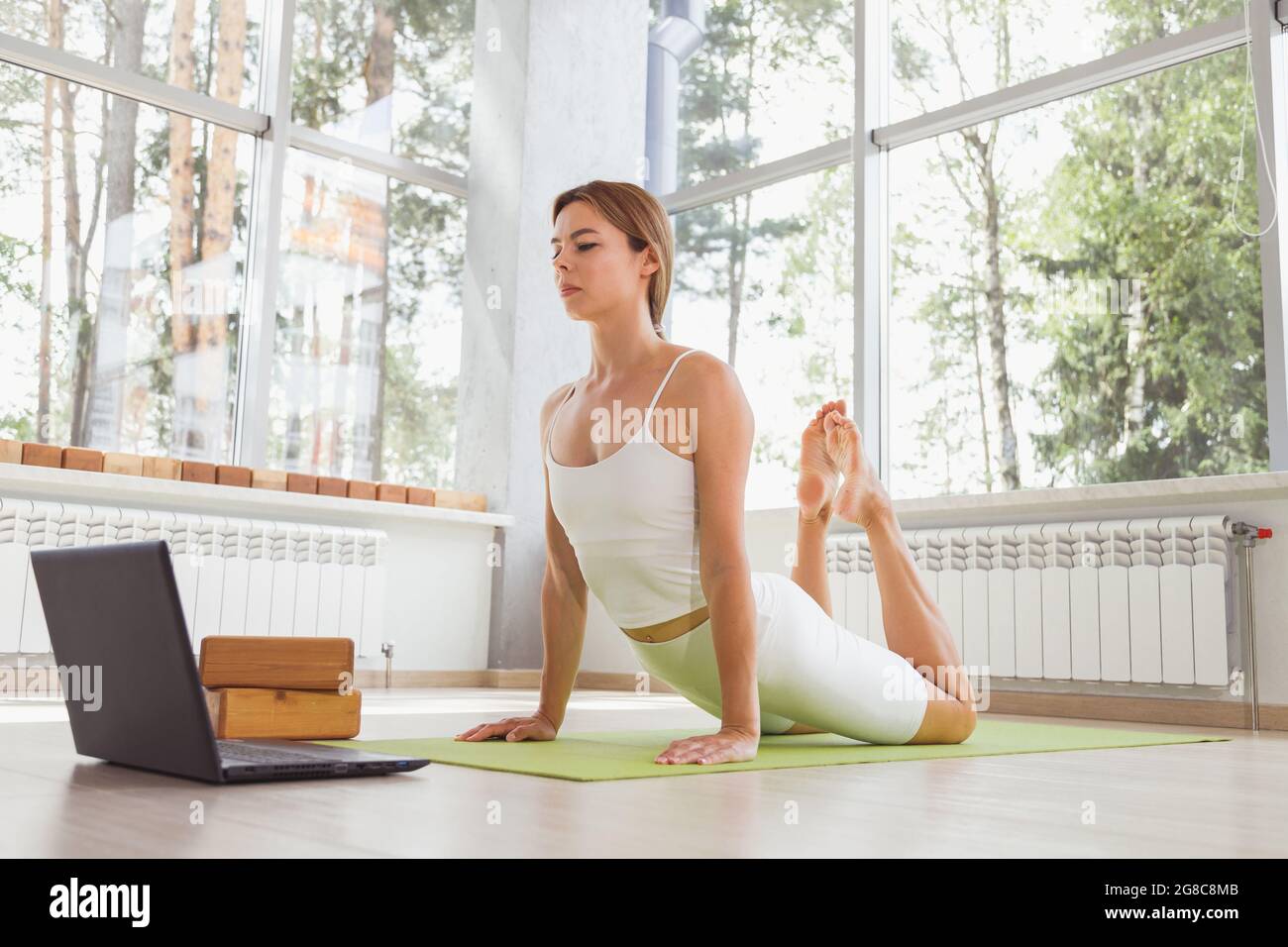 Giovane donna in forma sportiva che fa sport o yoga online con il laptop. Allenamenti a distanza, formatore online. Foto Stock