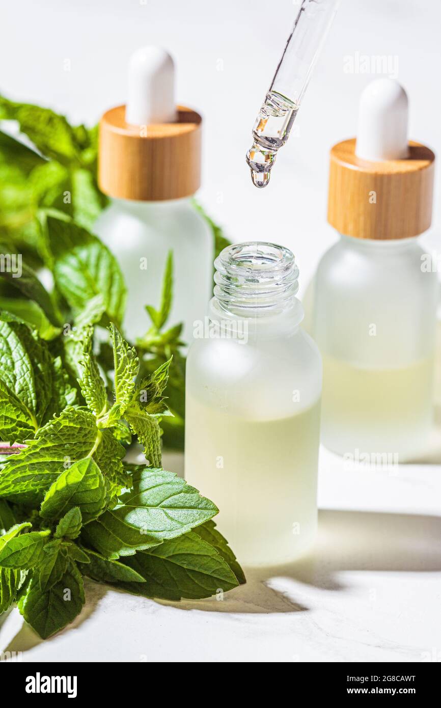 Olio essenziale alla menta in bottiglie di vetro, fondo in marmo bianco, primo piano. Concetto di cura della pelle e del corpo. Foto Stock