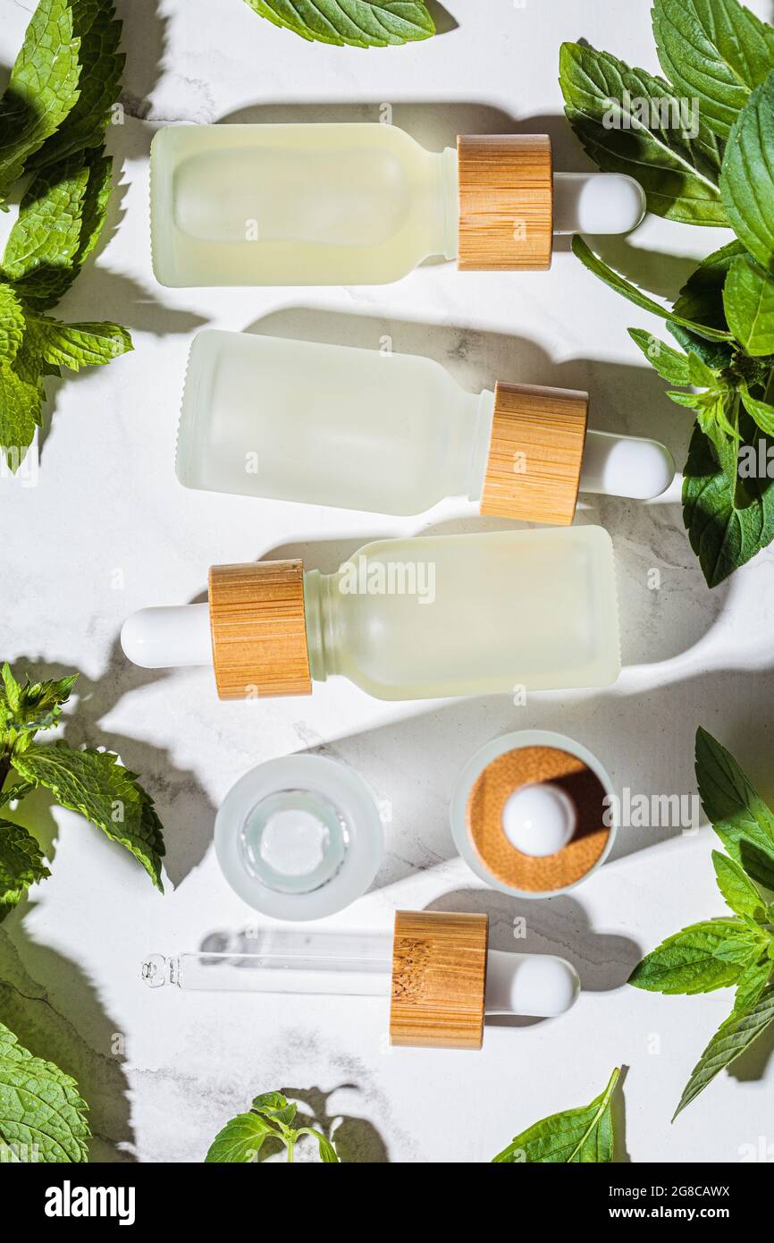 Olio essenziale menta in bottiglie di vetro, sfondo in marmo bianco, vista dall'alto. Concetto di cura della pelle e del corpo. Foto Stock