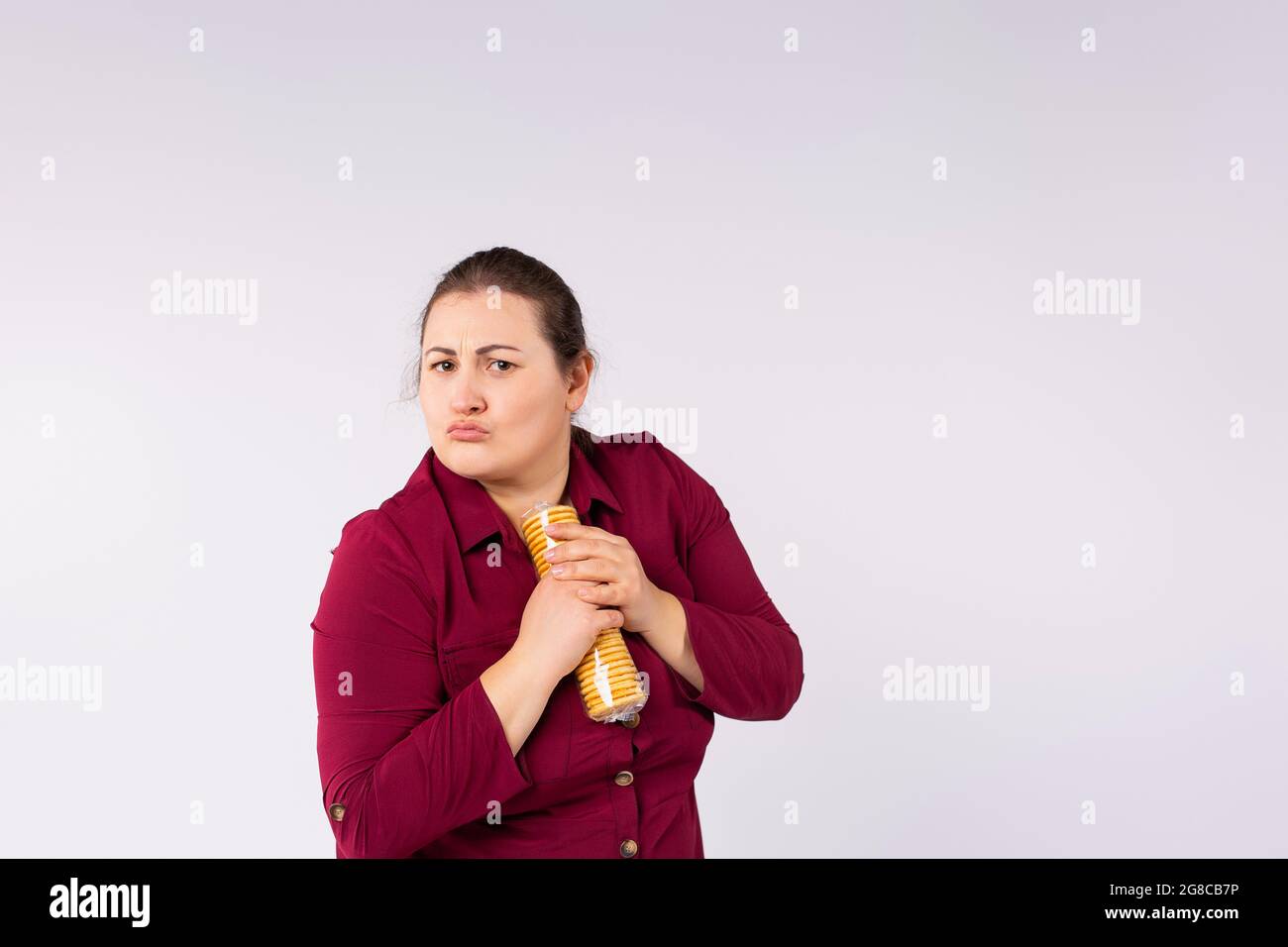Foto di una donna grassa seria in vestito rosso che tiene i biscotti di imballaggio nelle sue mani in modo da nessuno può prenderlo. Foto Stock