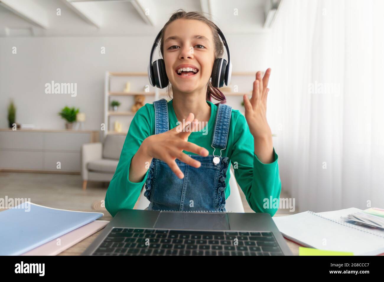 Ragazza che si siede alla scrivania e che ha una videochiamata indossando la cuffia Foto Stock