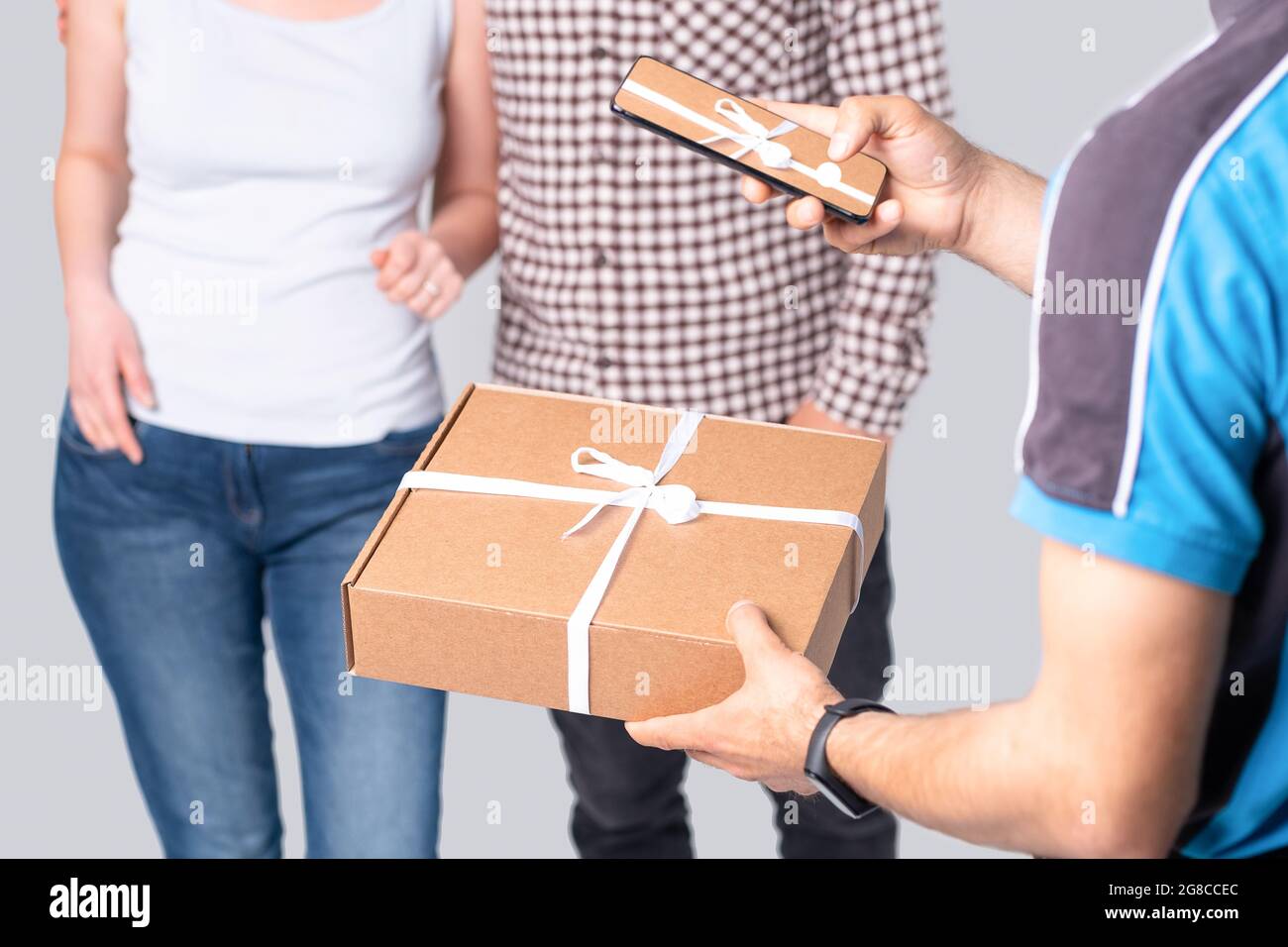Il corriere tiene lo smartphone mentre effettua la consegna e fa la foto di un pacco legato con un nastro bianco del regalo. Foto Stock