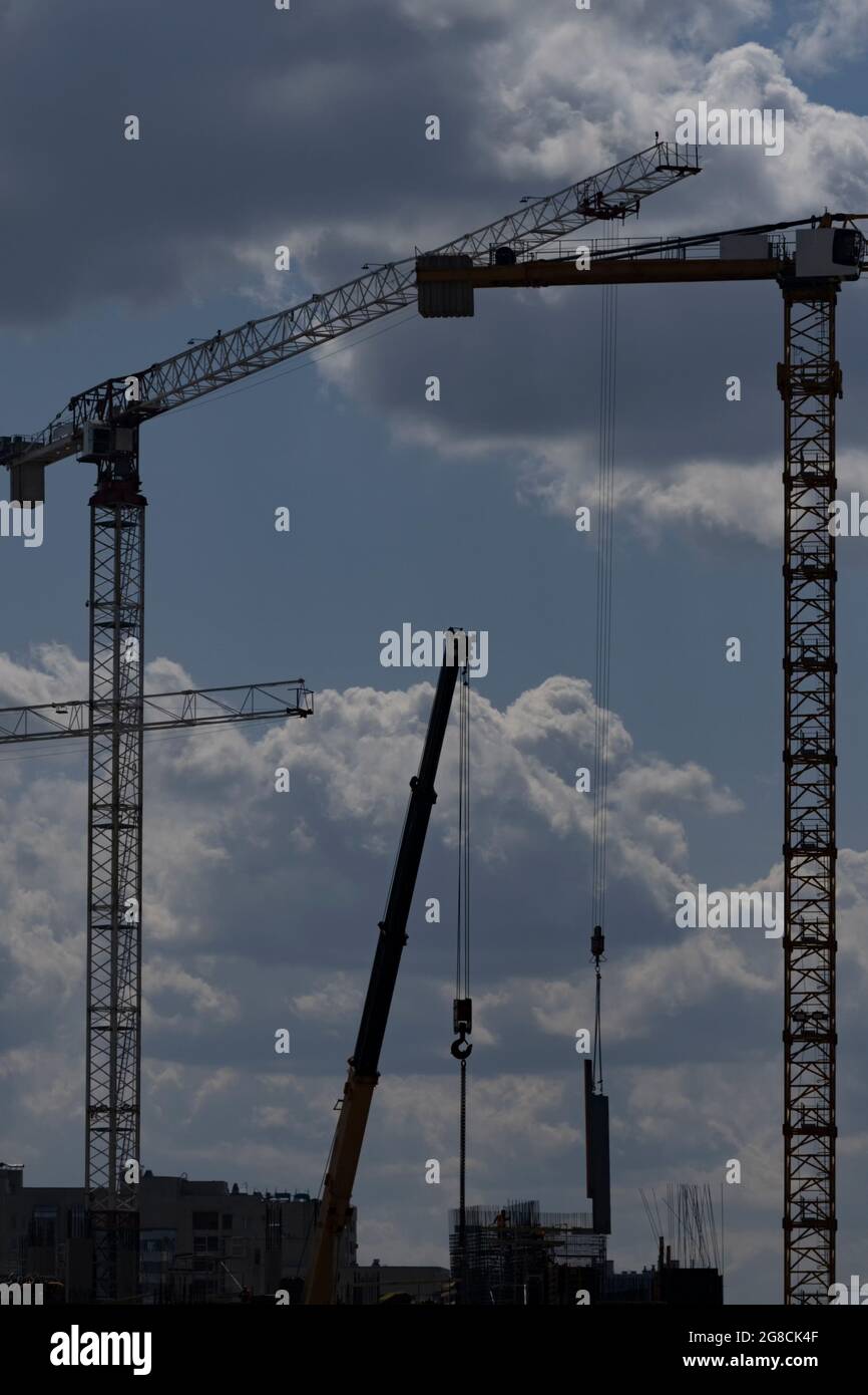 Due gru a torre e una gru ausiliaria sollevano i carichi sullo sfondo dell'orientamento verticale delle nuvole Foto Stock