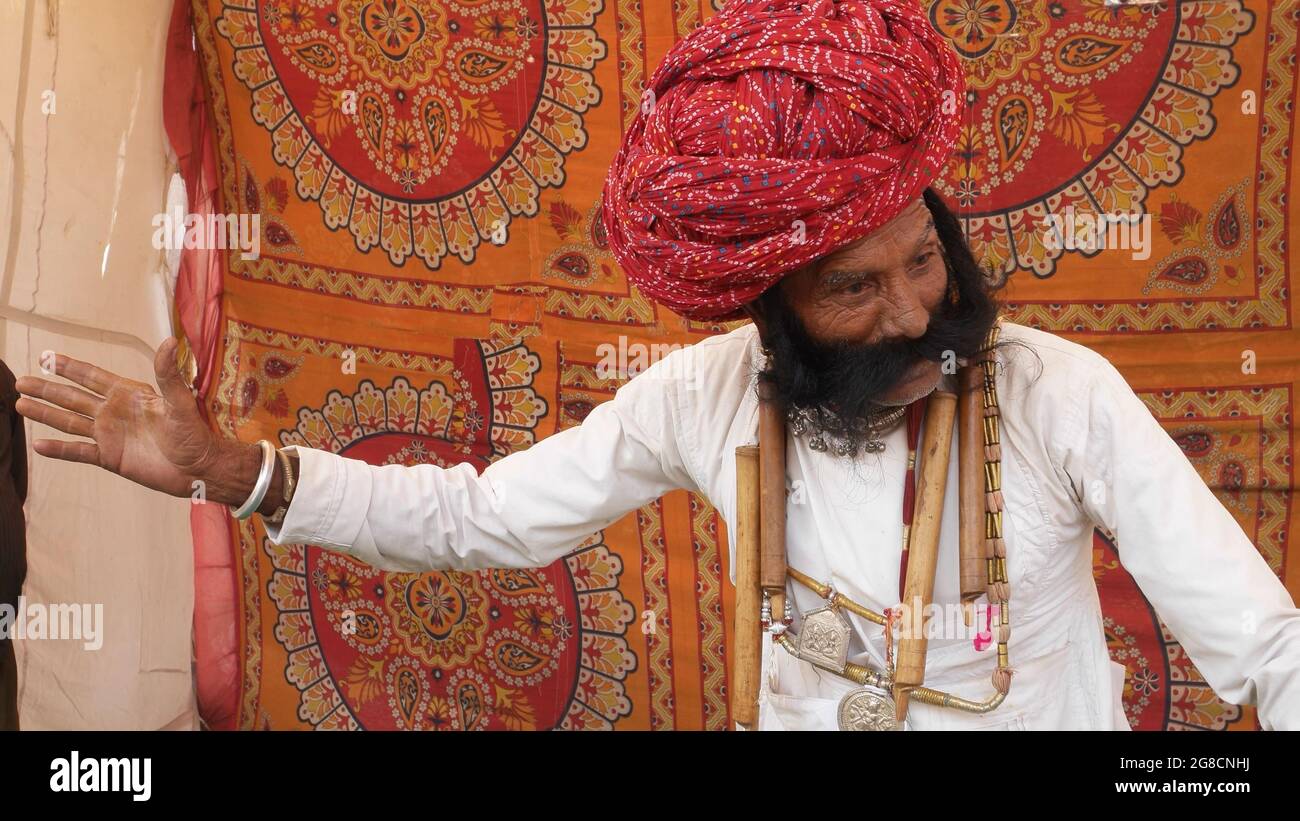 Vecchio maschio indiano che indossa abiti bianchi e un turbante rosso in piedi sullo sfondo modellato Foto Stock