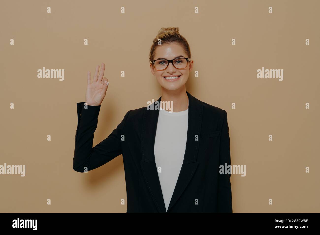 Positivo giovane donna caucasica in classico indossare isolato su sfondo beige mostrando ok segno Foto Stock