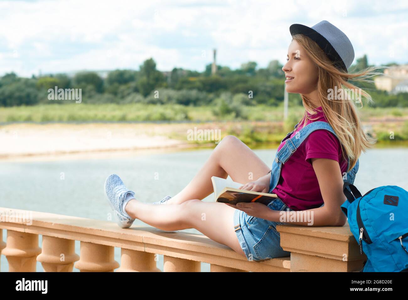 Grazioso studente seduto con un libro vicino al fiume. Foto Stock