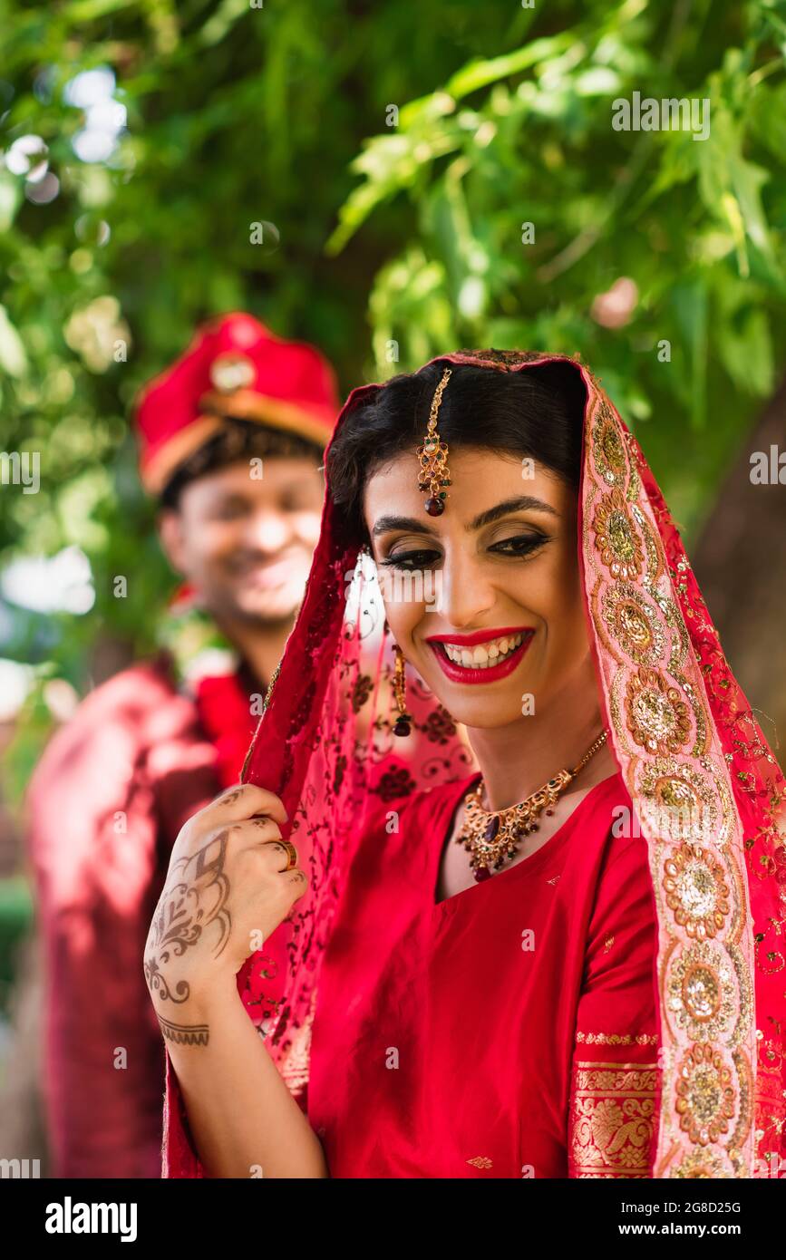 sorridente sposa indiana in sari e velo vicino uomo offuscato in turbante  sullo sfondo Foto stock - Alamy