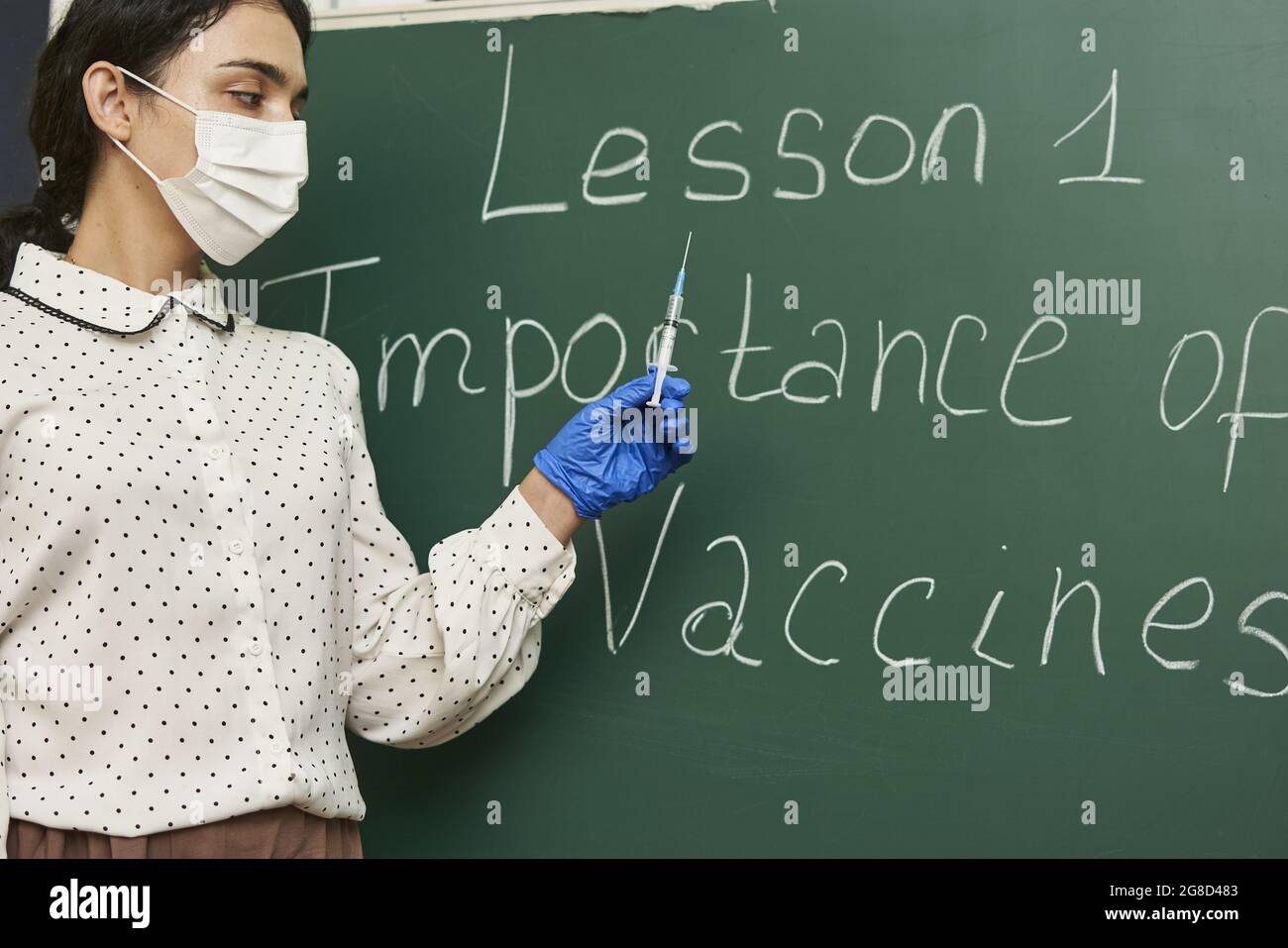 Insegnante che indossa un facemask e insegna sull'importanza dei vaccini per la classe Foto Stock