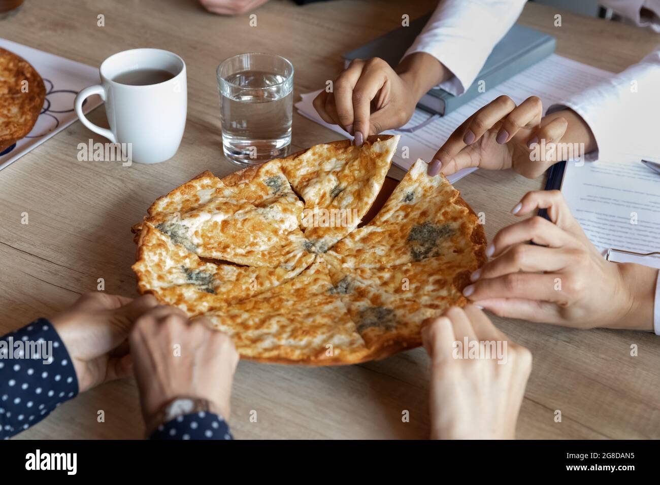 Pizza calda sul tavolo da ufficio, mani di dipendenti che prendono le fette Foto Stock