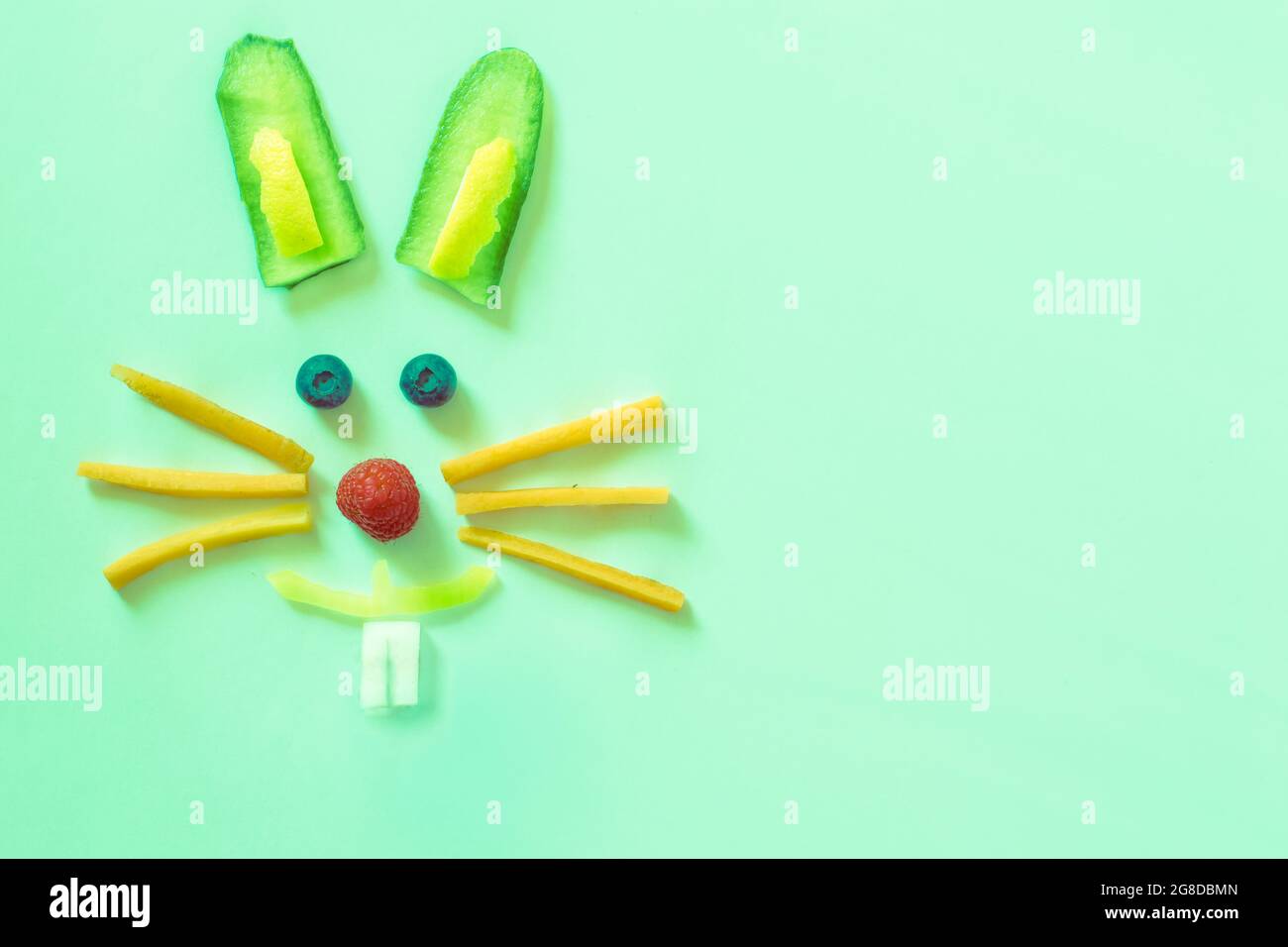 Faccia di coniglio fatta da pezzi di frutta e verdura, isolata su sfondo verde, concetto di Pasqua felice Foto Stock