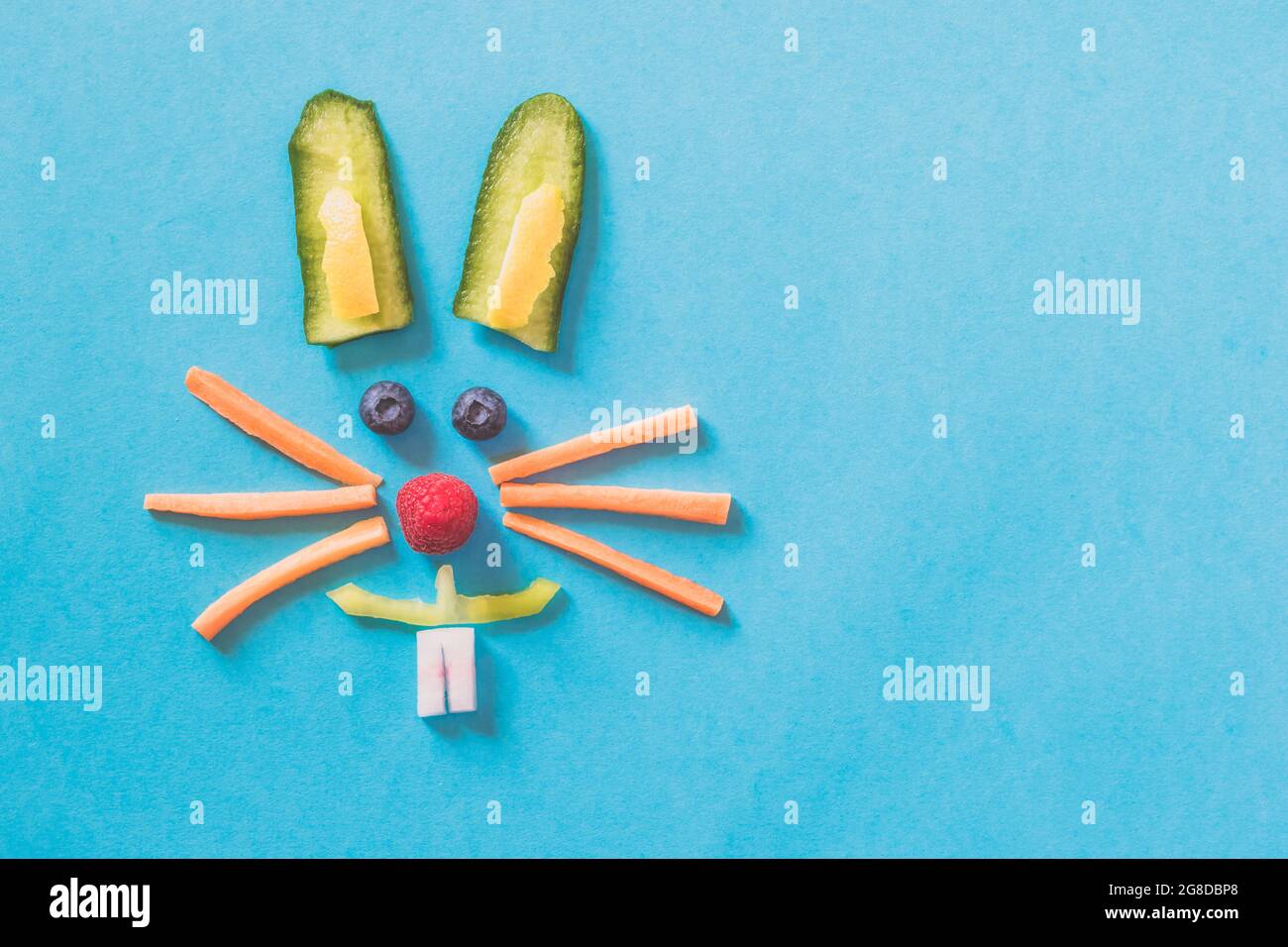 Faccia di coniglio fatta da pezzi di frutta e verdura, isolata su sfondi blu, concetto di Pasqua felice Foto Stock