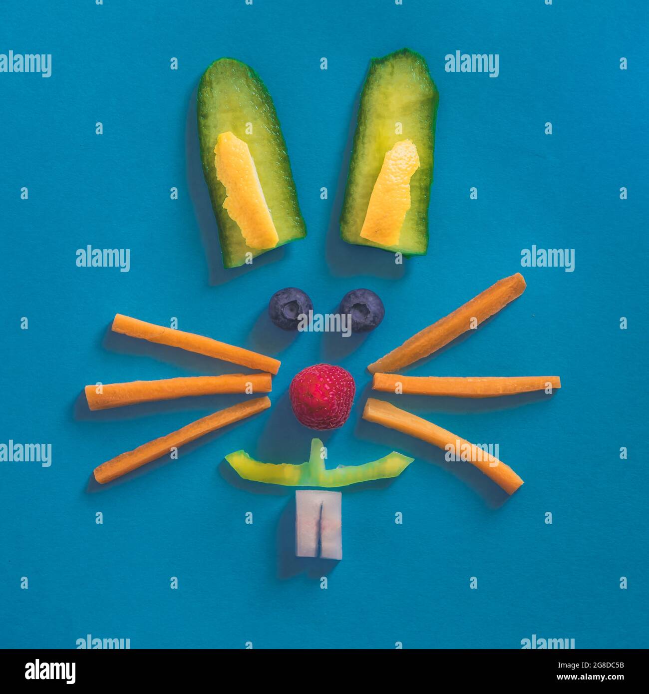 Faccia di coniglio fatta da pezzi di frutta e verdura, isolata su sfondi blu, concetto di Pasqua felice Foto Stock