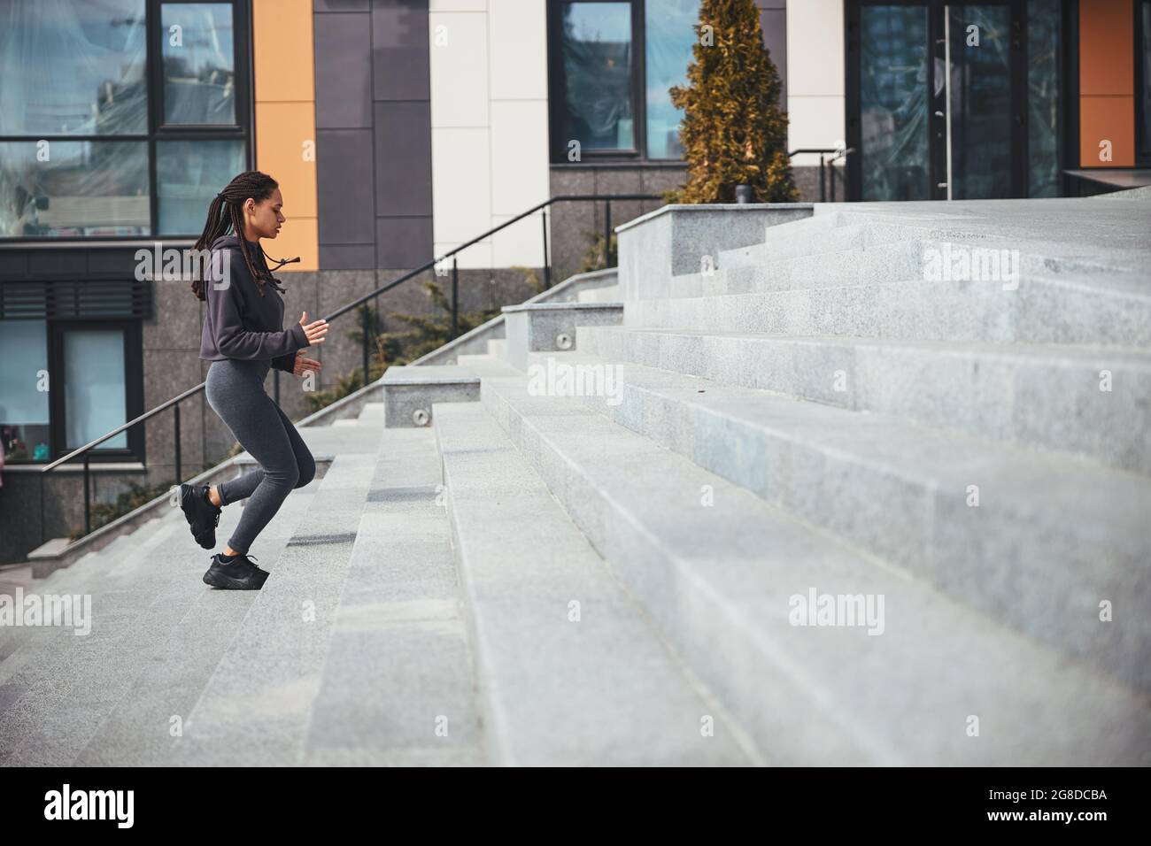 Sportiva con grappoli afro alla moda che salgono i gradini di cemento Foto Stock