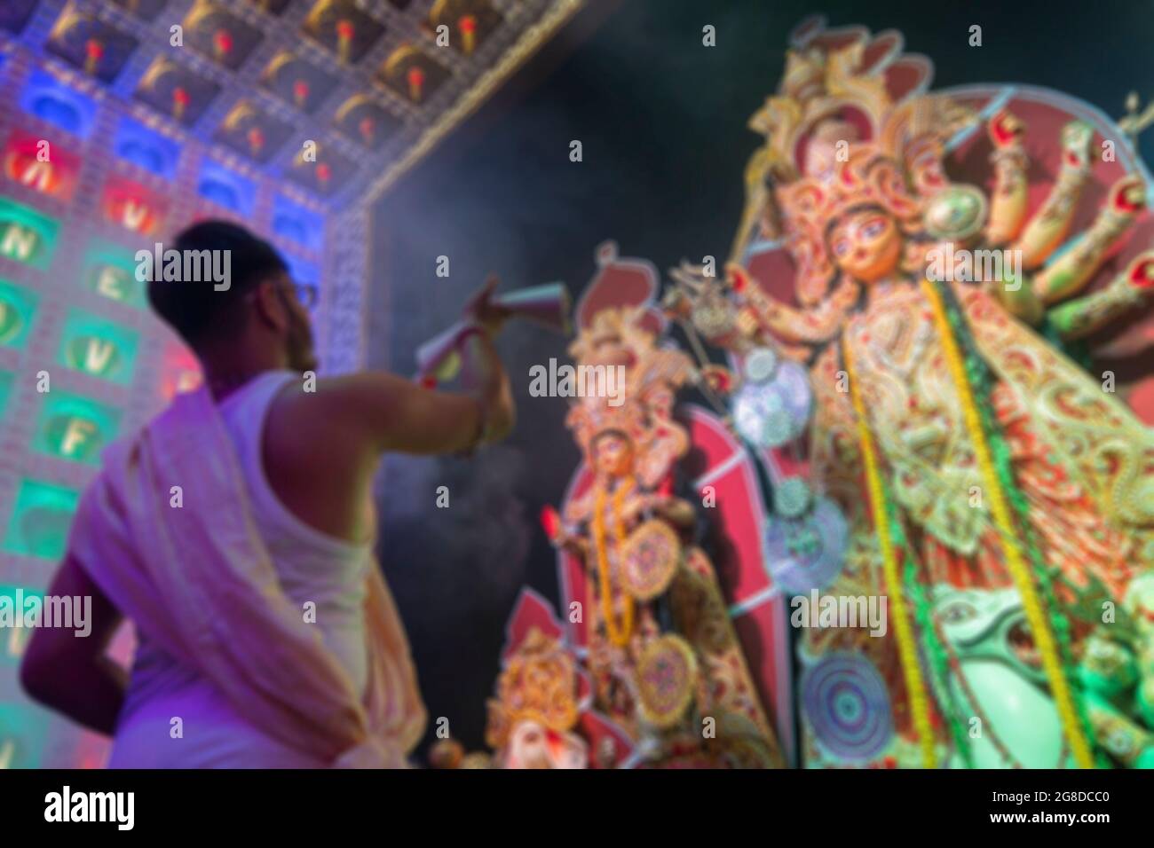 Immagine offuscata di Purhit indù bengalese che offre Dea Durga uno shari, abito tradizionale indiano donna, sotto fumo Santo durante Durga Puja . Ripresa da Foto Stock