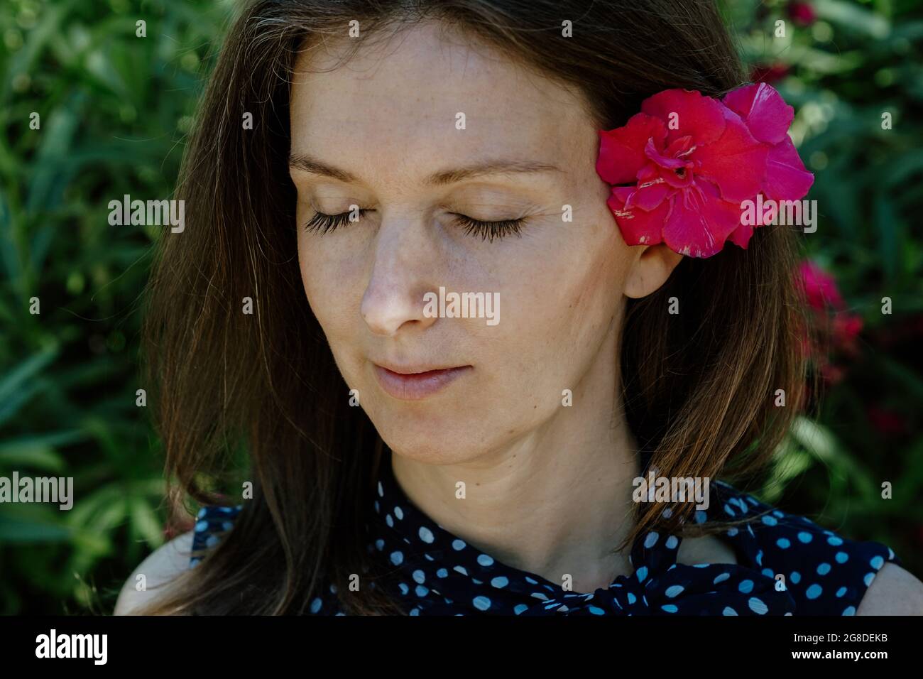 Donna spagnola con un fiore tra i capelli, con occhi chiusi, gode dell'atmosfera rilassante del giardino Foto Stock