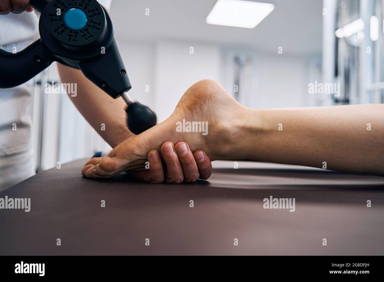 Primo piano di massaggiatore sfregamento piede donna con dispositivo di percussione massaggio in sala di terapia delle cliniche di riabilitazione Foto Stock