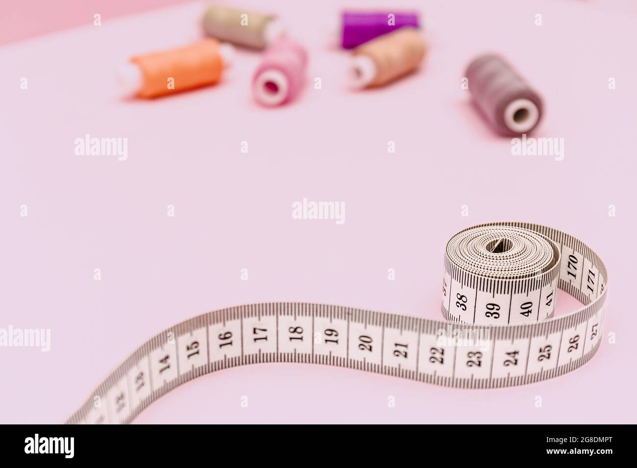Fondo di cucitura con nastro di misurazione su sfondo rosa. Accessori di sarto o marinaio. Fili da cucire, aghi, tessuti, centimetro di cucitura o m Foto Stock
