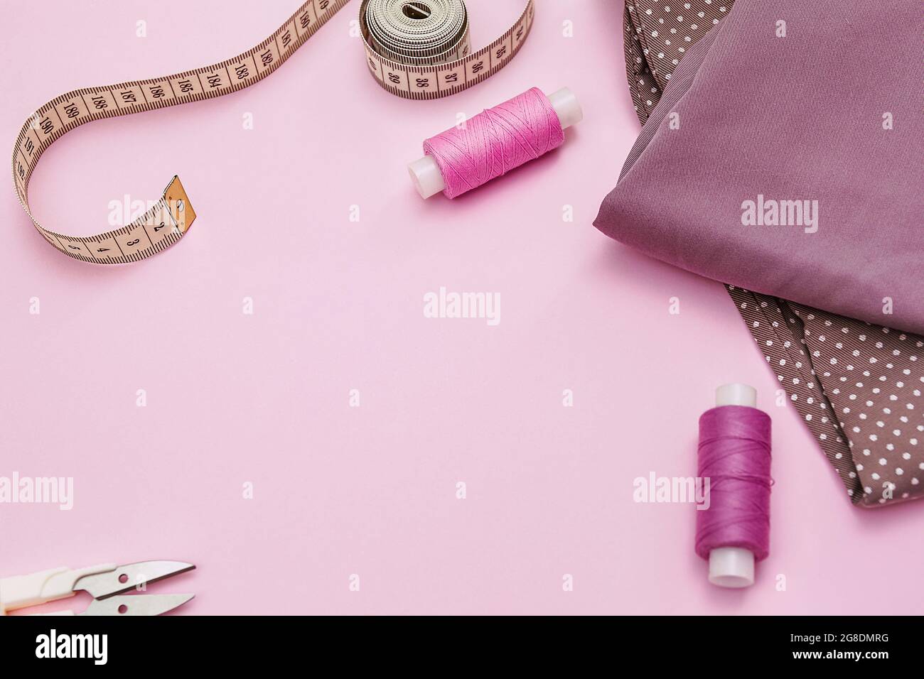 Scrivania su misura. Accessori per cucire e tessuto su sfondo rosa. Fili da cucire, aghi, tessuti, centimetro da cucire o nastro di misurazione. Foto Stock