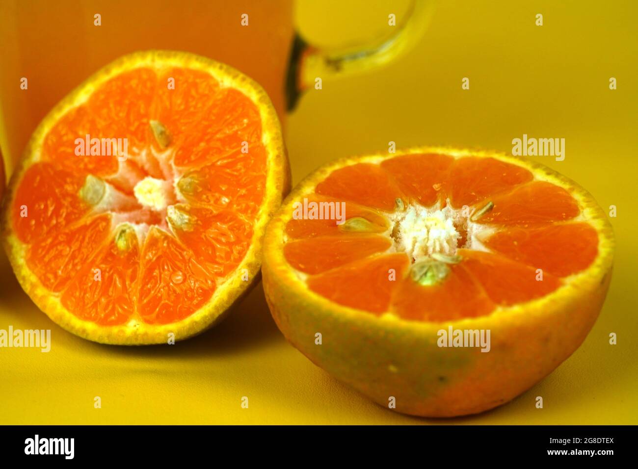 Primo piano di due metà di un'arancia con succo d'arancia fresco sul retro su sfondo giallo Foto Stock