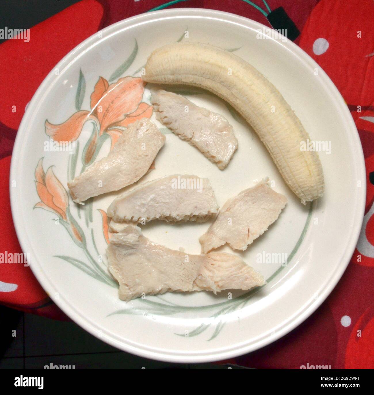 Cibo piatto dieta di fette di pollo magre e una banana su un piatto crema con un modello di grano Foto Stock