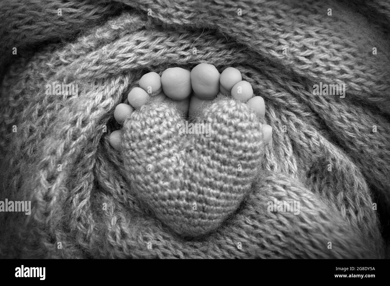 Piedi di un neonato con un cuore di legno, avvolto in una morbida coperta. Bianco-nero. Foto Stock