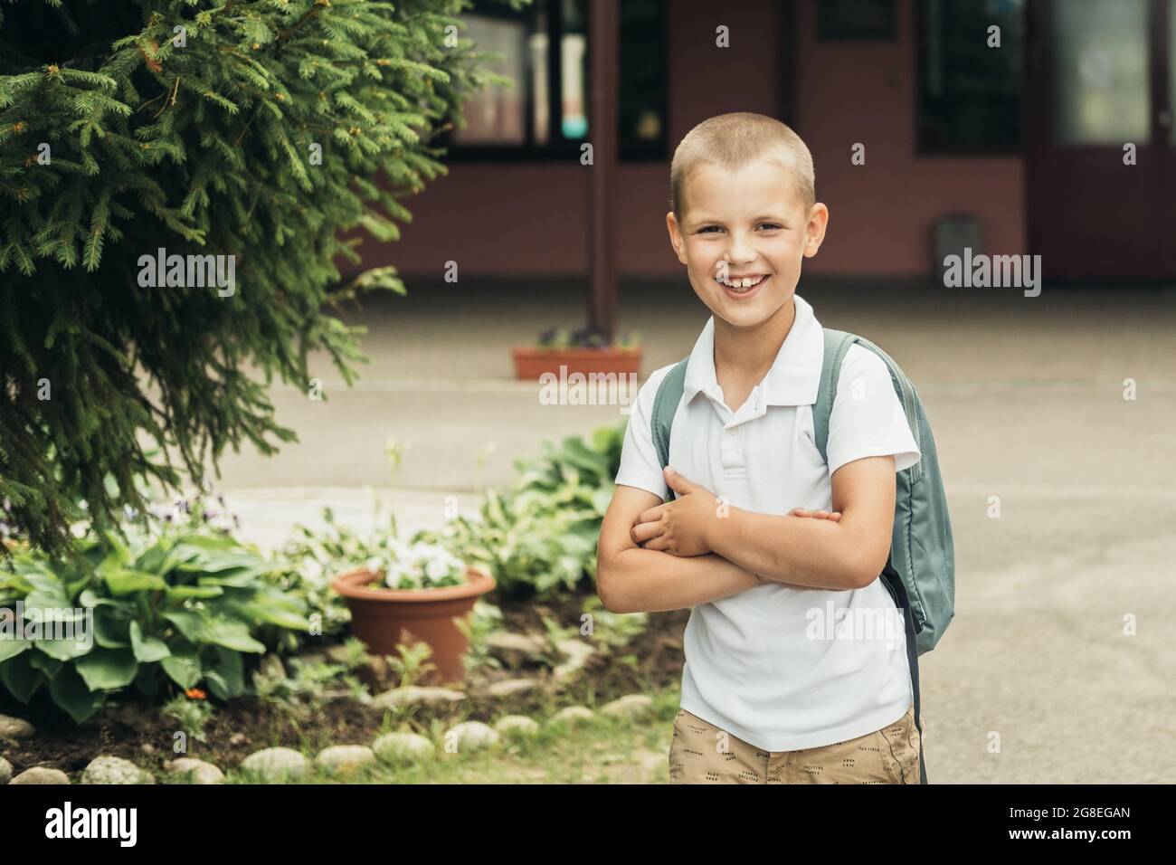 Ragazzo sorridente, studente di scuola elementare, che cammina a scuola con la borsa dietro la schiena. Foto Stock