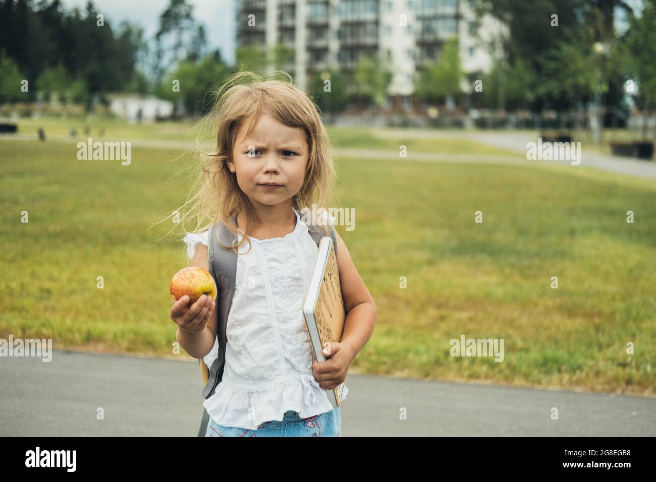 La ragazza carina, studente di scuola elementare, a piedi a scuola con borsa dietro, libro e mela. Gli studenti sono pronti per il nuovo anno. Ritorno a scuola. Foto Stock