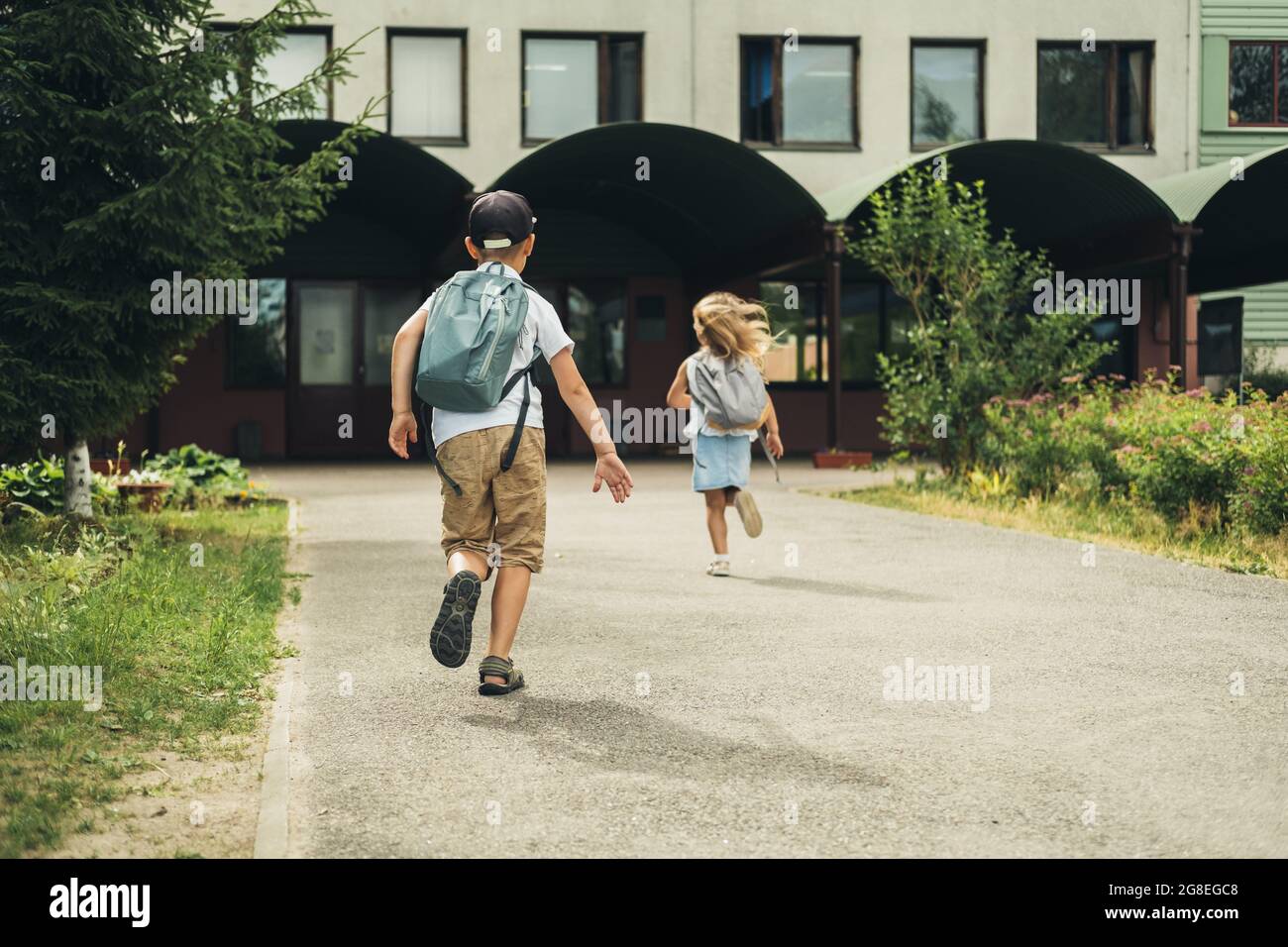 Due bambini caucasici, ragazzo e ragazza, corrono a scuola con borse dietro le spalle. Gli studenti sono pronti per il nuovo anno. Ritorno a scuola. Foto Stock