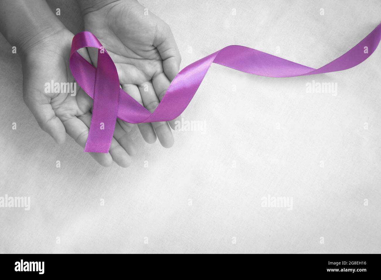 Mani che tengono il nastro viola o viola su tessuto bianco con spazio per la copia. Cancro pancreatico, consapevolezza del cancro testicolare, sopravvivenza del cancro, Leiomiosarcoma Foto Stock