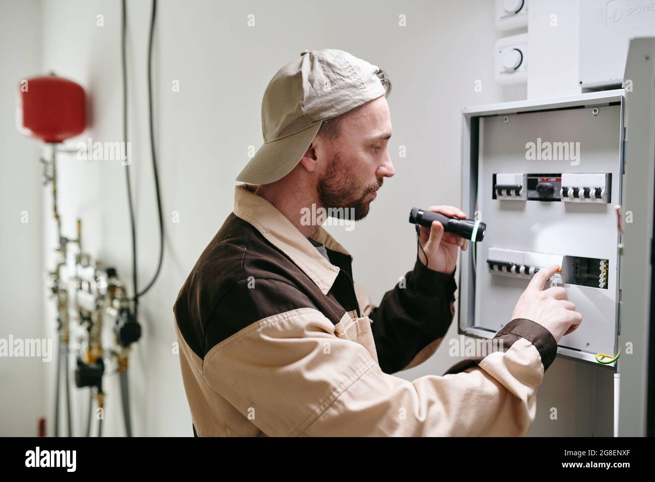 Giovane elettricista che controlla gli interruttori sul pannello di tensione durante il lavoro Foto Stock