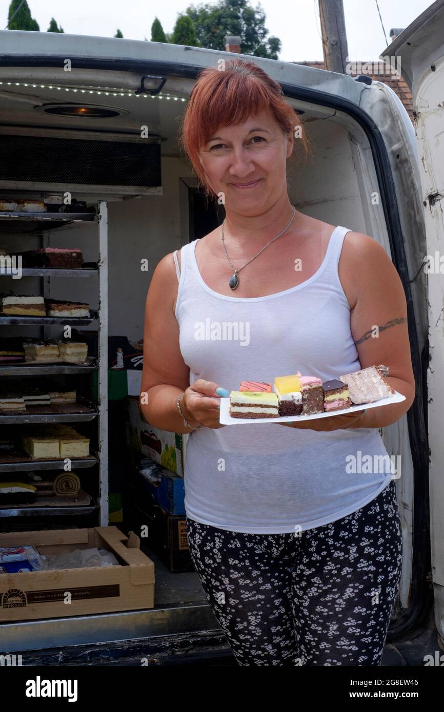sorriing femmina vassoio di contenimento con selezione di torte accanto al suo mobile torta consegna van in piccolo villaggio rurale zala contea ungheria Foto Stock