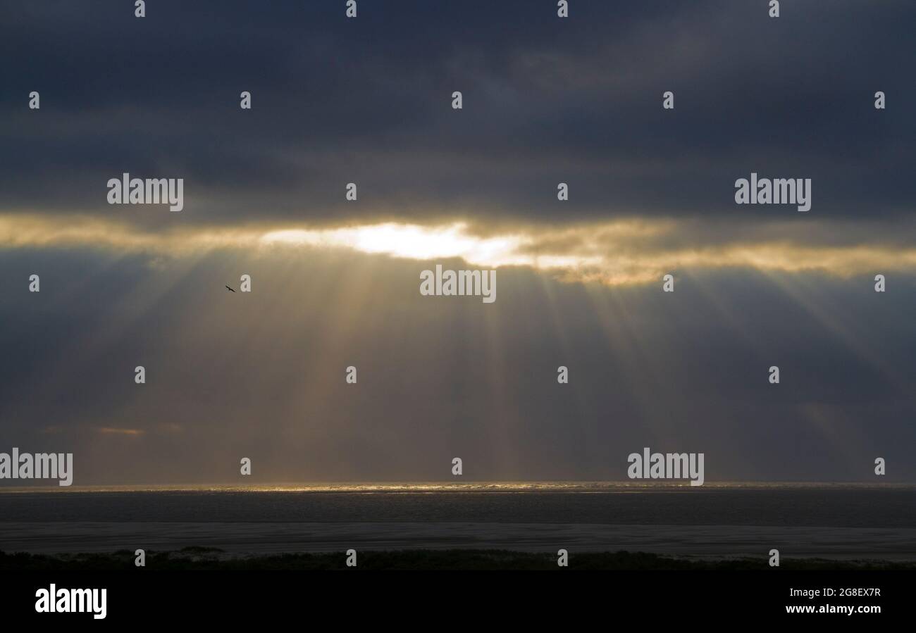 Raggi di sole da un cielo scuro e nuvoloso sopra un mare scuro Foto Stock