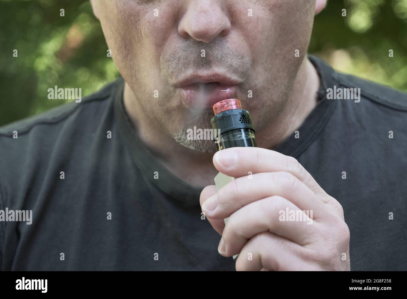 Faccia di un uomo che fuma una sigaretta elettronica. Uomo che tiene il dispositivo di evaporazione ed espala il fumo. Vaporizzare un liquido per inalare Foto Stock