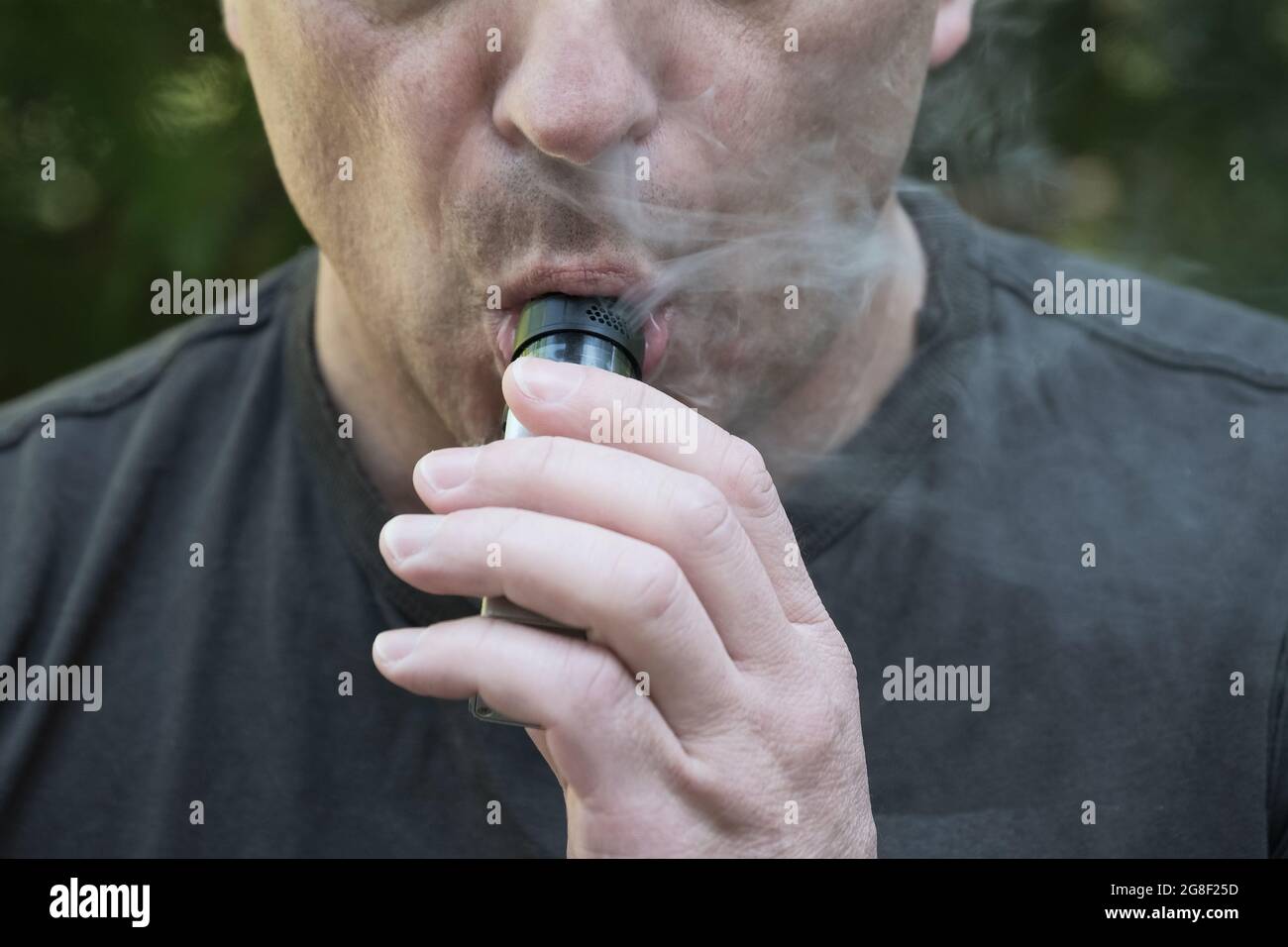 Primo piano di un uomo che fuma una sigaretta elettronica. L'uomo tiene il dispositivo di evaporazione e inala il fumo. Vaporizzare un liquido per inalare Foto Stock
