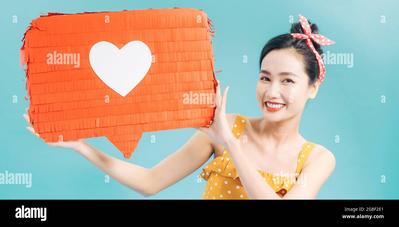 bella ragazza sorridente che tiene carta rossa con il simbolo del cuore e guardando la macchina fotografica isolata su blu Foto Stock