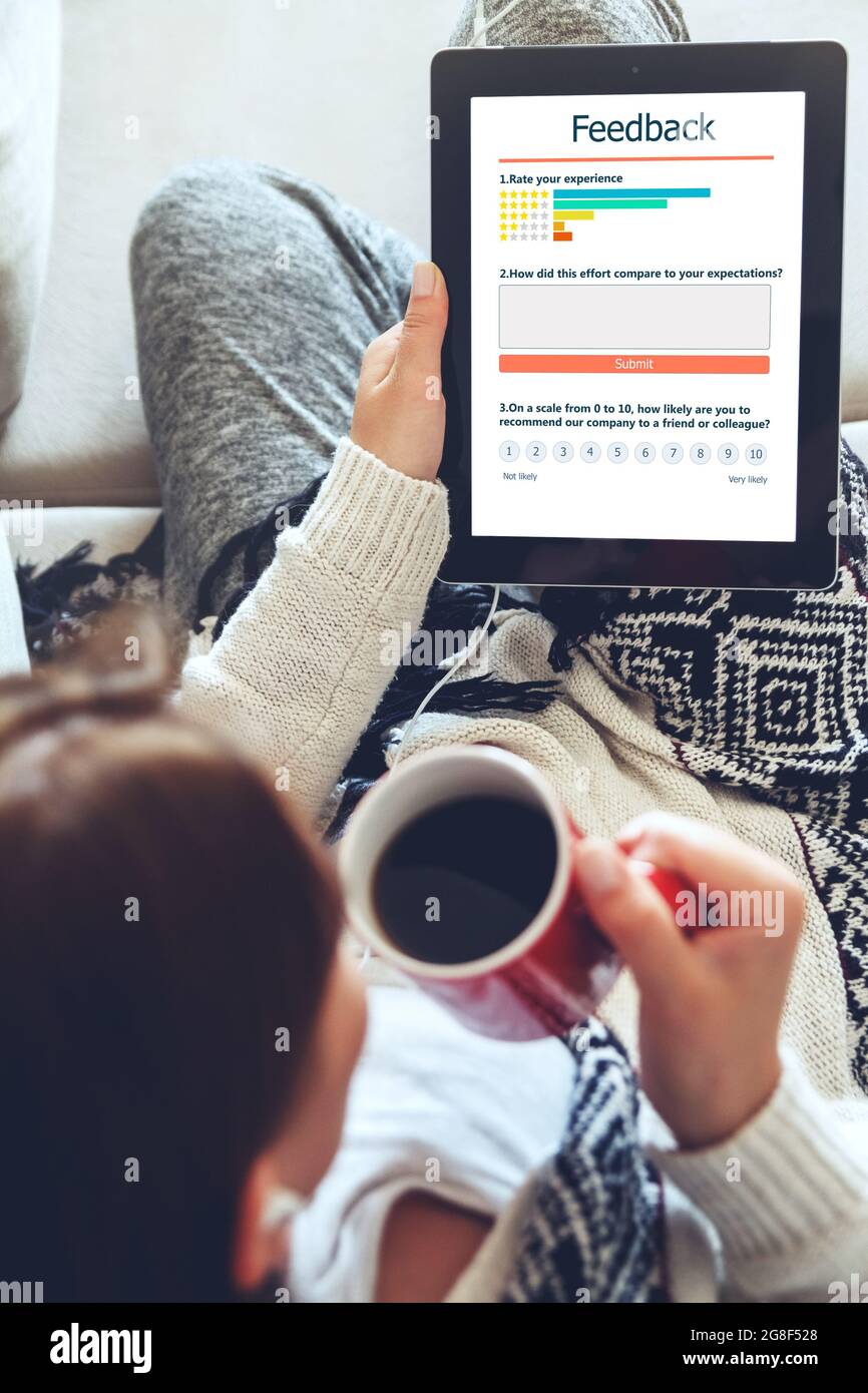 La giovane donna scrive una recensione del cliente e lascia la valutazione sul tablet. Esperienza del cliente e concetto di feedback. Foto Stock