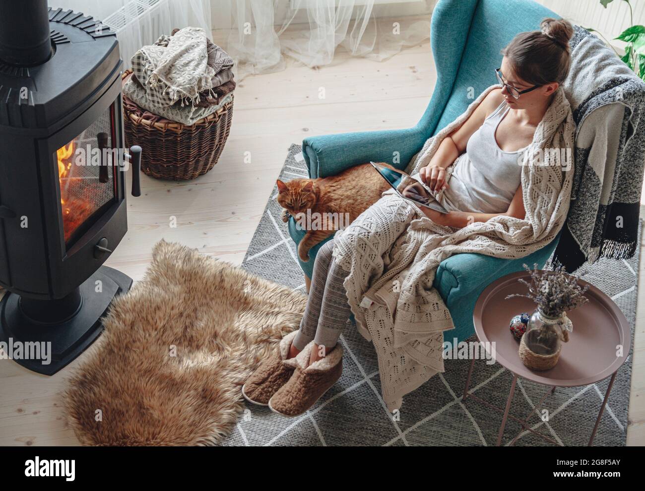 donna accanto al camino, seduta in una comoda poltrona, con un caldo Foto Stock
