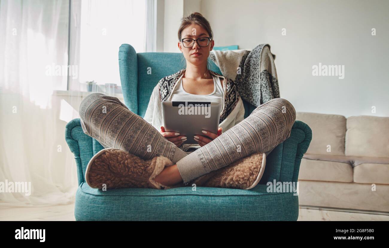 donna seduta in comoda poltrona, con coperta calda, con tablet Foto Stock