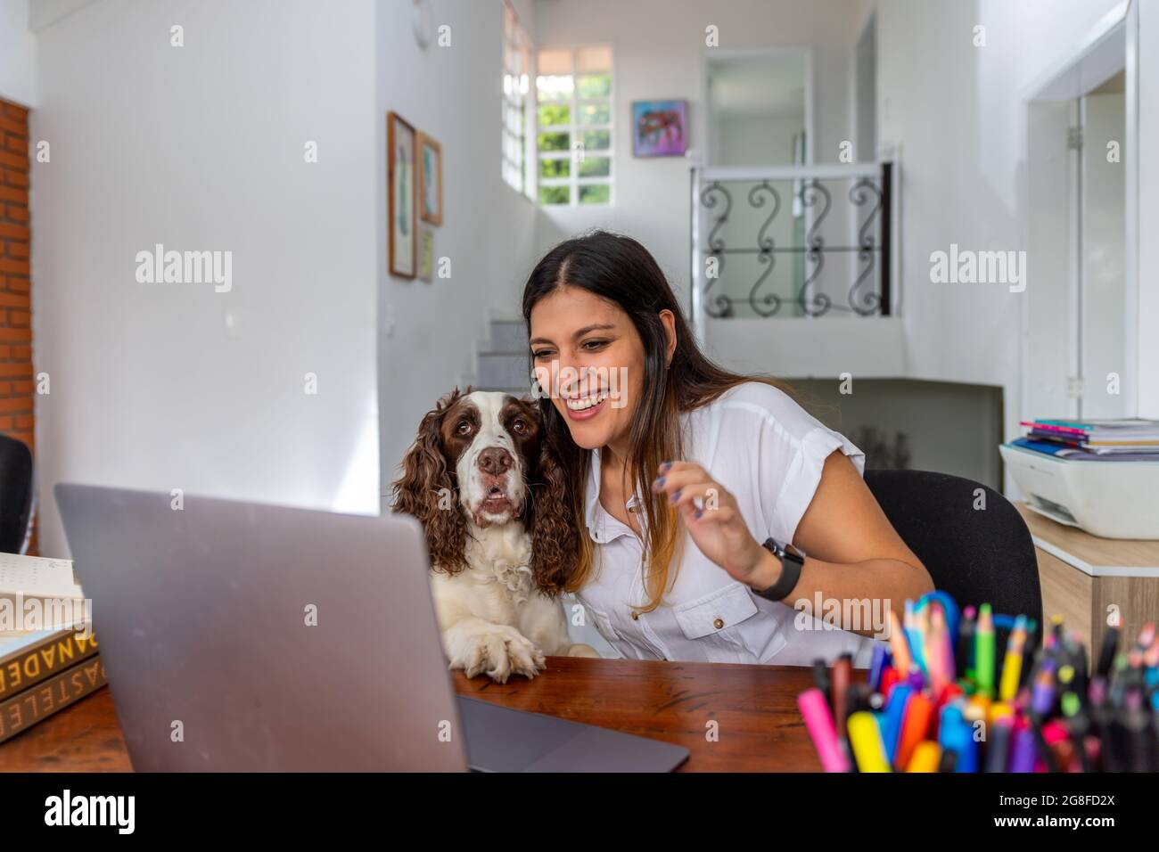 Donna latina sorridente che ha videochiamata via laptop in ufficio domestico mostrando il suo cane Foto Stock